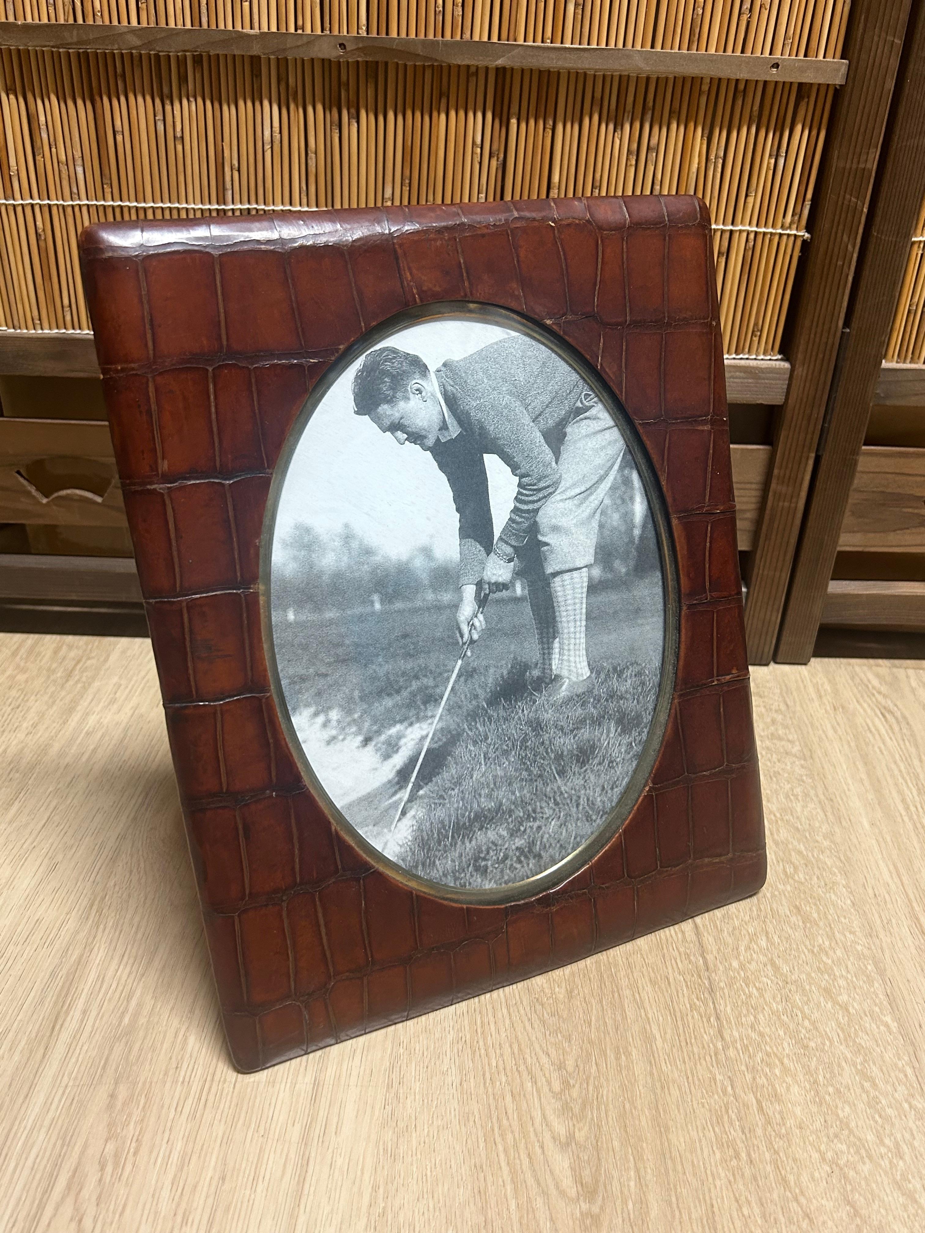The front of the frame is covered in alligator leather and trimmed in brass along the circumference of the oval opening. The back is covered with oiled canvas and the inside lined with original golden fabric. The photo in it is a simple reproduction