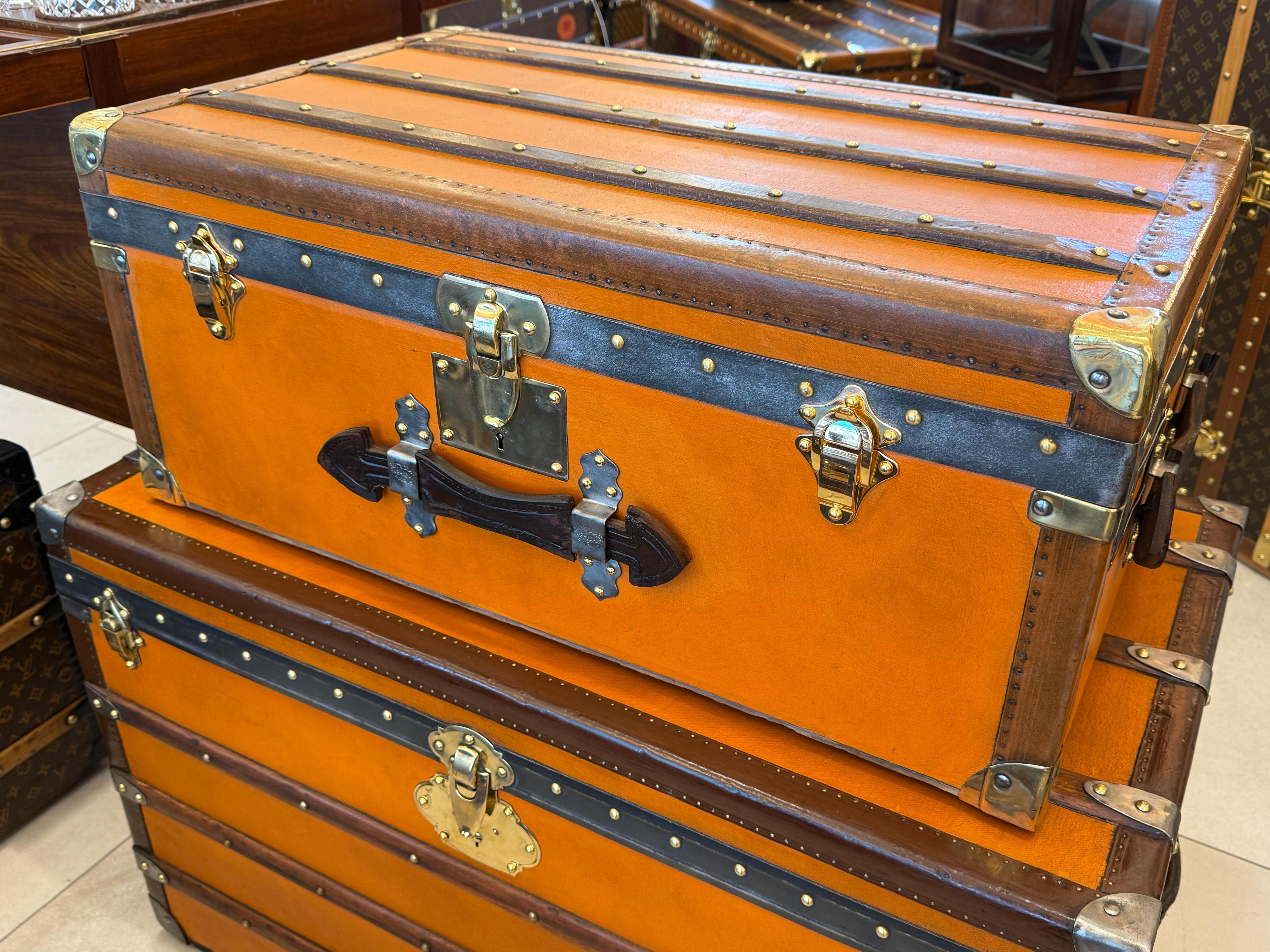 Cette petite malle à vapeur de Moynat présente une très belle et très recherchée toile orange ainsi que des coins en laiton massif, 1 serrure et 2 fermoirs en laiton, deux grandes poignées latérales en cuir et une autre sur le devant avec des