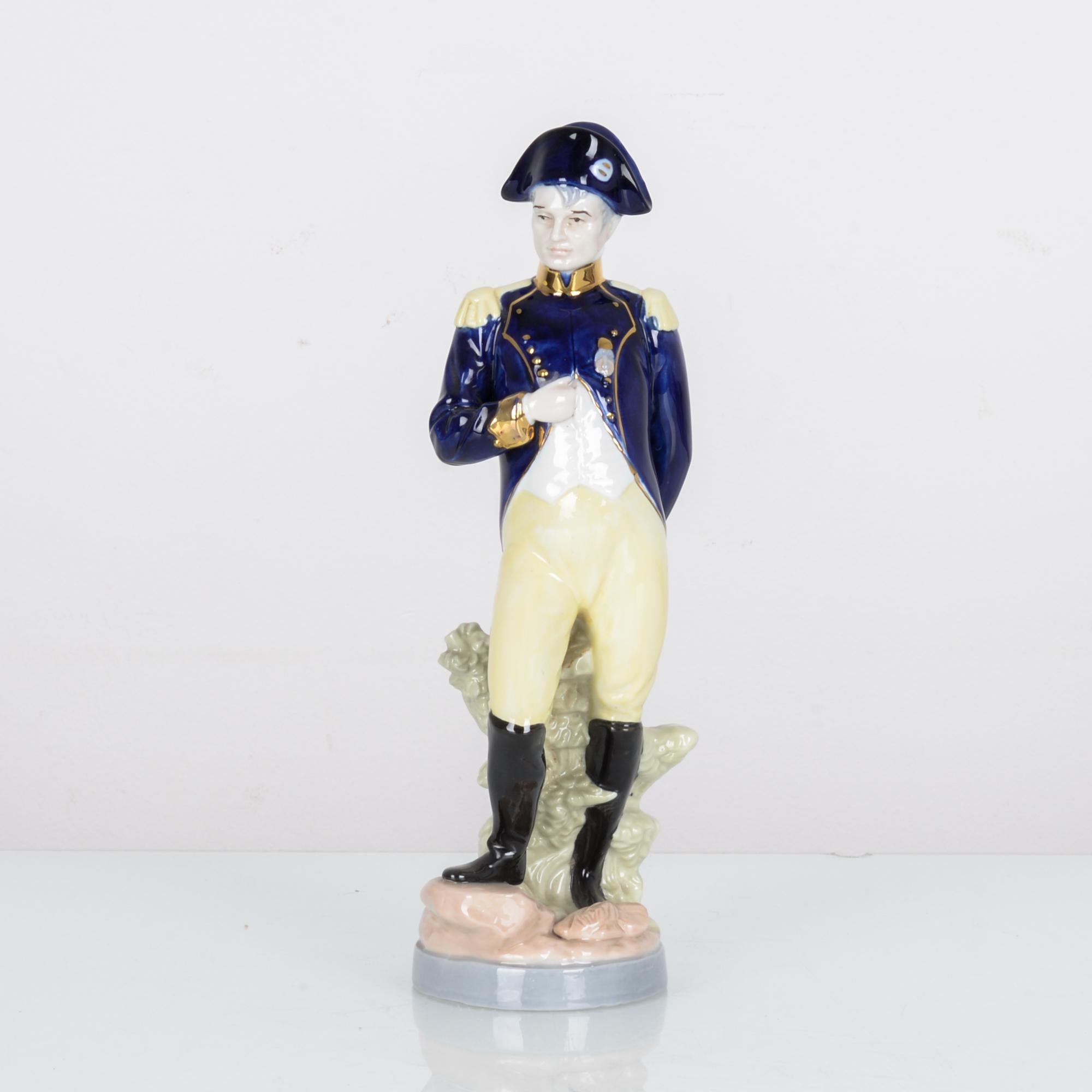 This hand painted ceramic figurine was made in France, circa 1920. The figure of Napoleon stands with one hand in his waistcoat, a gesture associated with assurance and nobility. The deep cobalt blue of his hat and jacket stands out against the