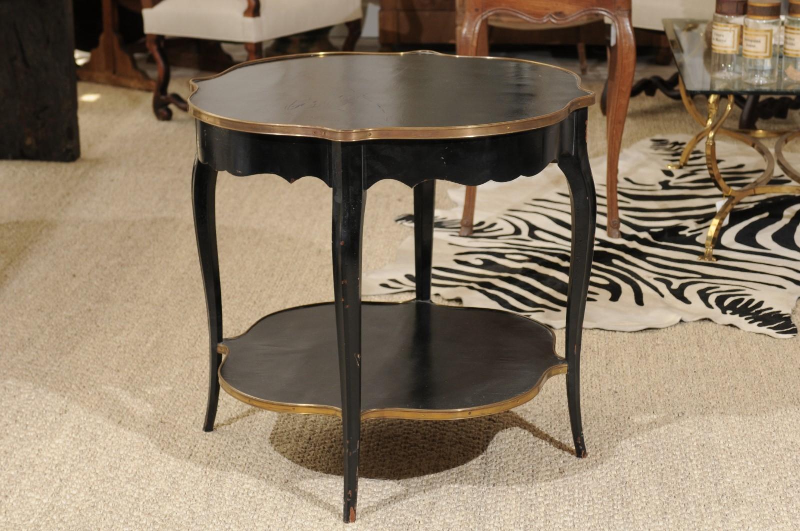 A French Napoleon III style black-painted quatrefoil side table from the early 20th century, with gold accents, scalloped apron and lower shelf. A very unusual, quatrefoil-shaped French table with black paint and gold detailing. Its elegant lines