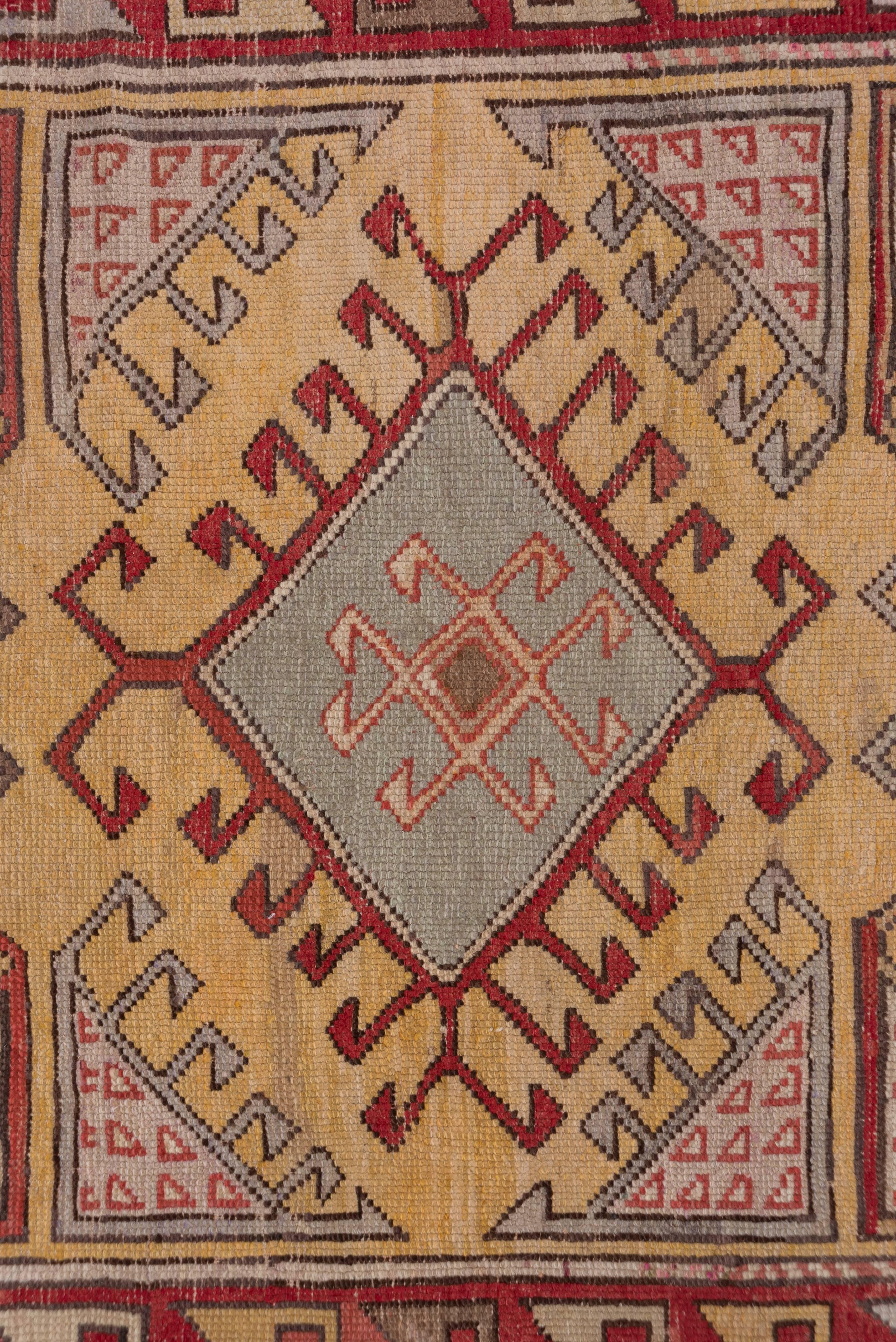 The yellow ground of this Anatolian runner is decorated by hooked lozenge medallions in red, ivory & pistachio. There are additional hooked triangle filters in at the sides of the field. The red main border has a stylized S Pattern.