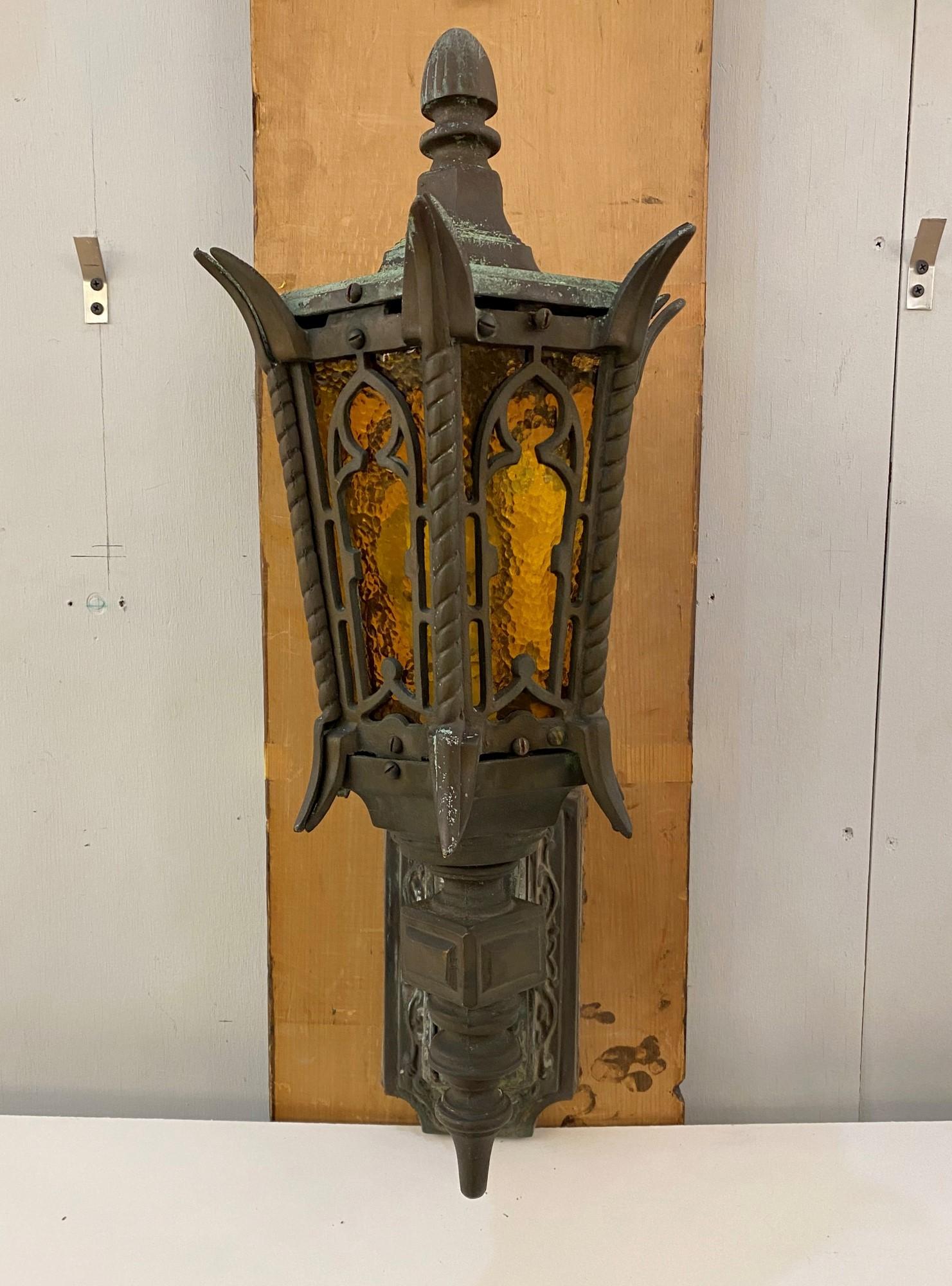 1920s pair of Gothic Tudor exterior bronze sconces with original verdigris patina and featuring textured amber glass shades. This can be seen at our 333 West 52nd St location in the Theater District West of Manhattan.