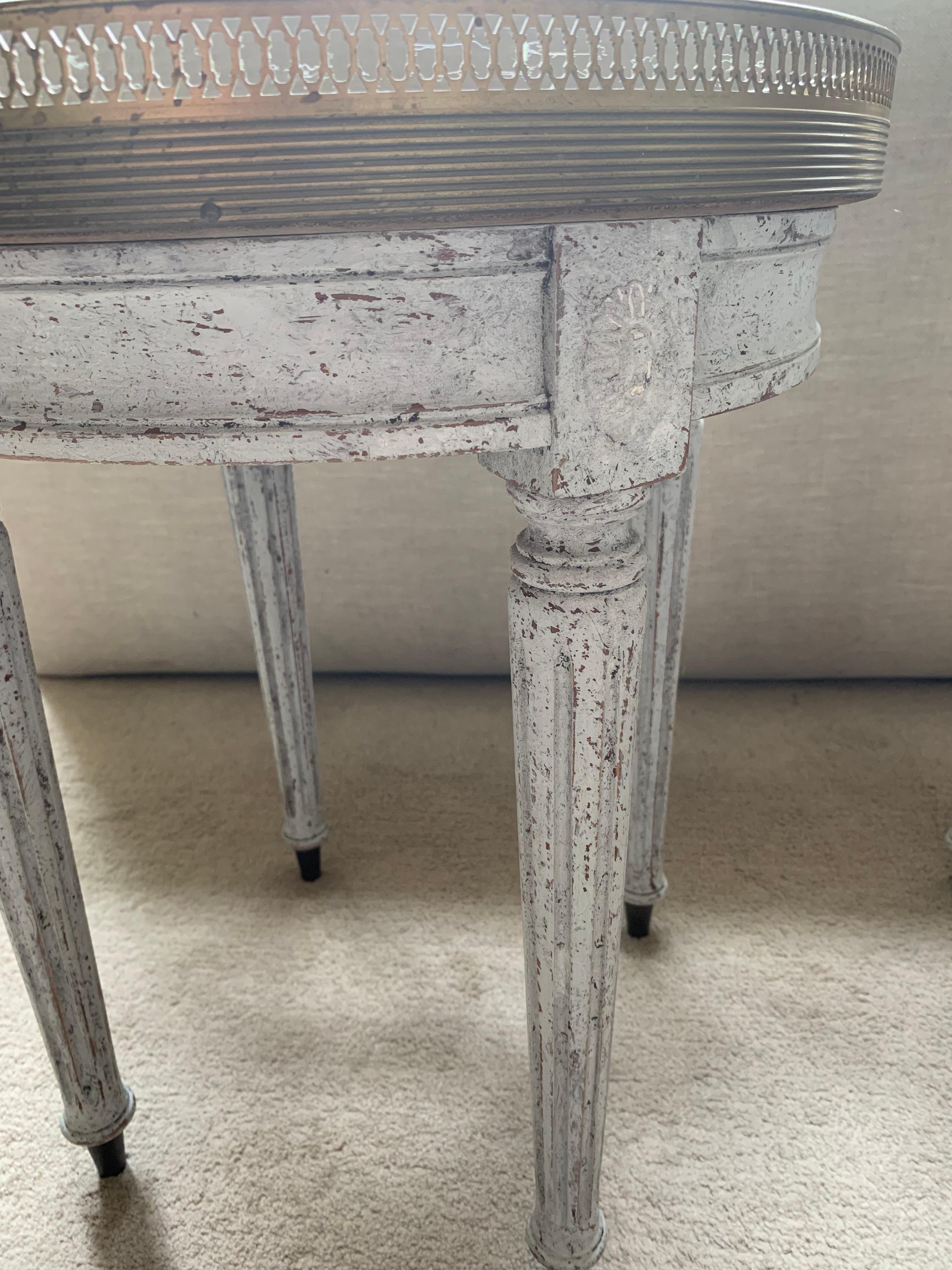 A handsome pair of circa 1920s Scandinavian painted side tables with marble tops banded with reeded brass with fretwork gallery surround.
In a striking mottled grey green marble they sit firmly on four later painted pale grey fluted legs with