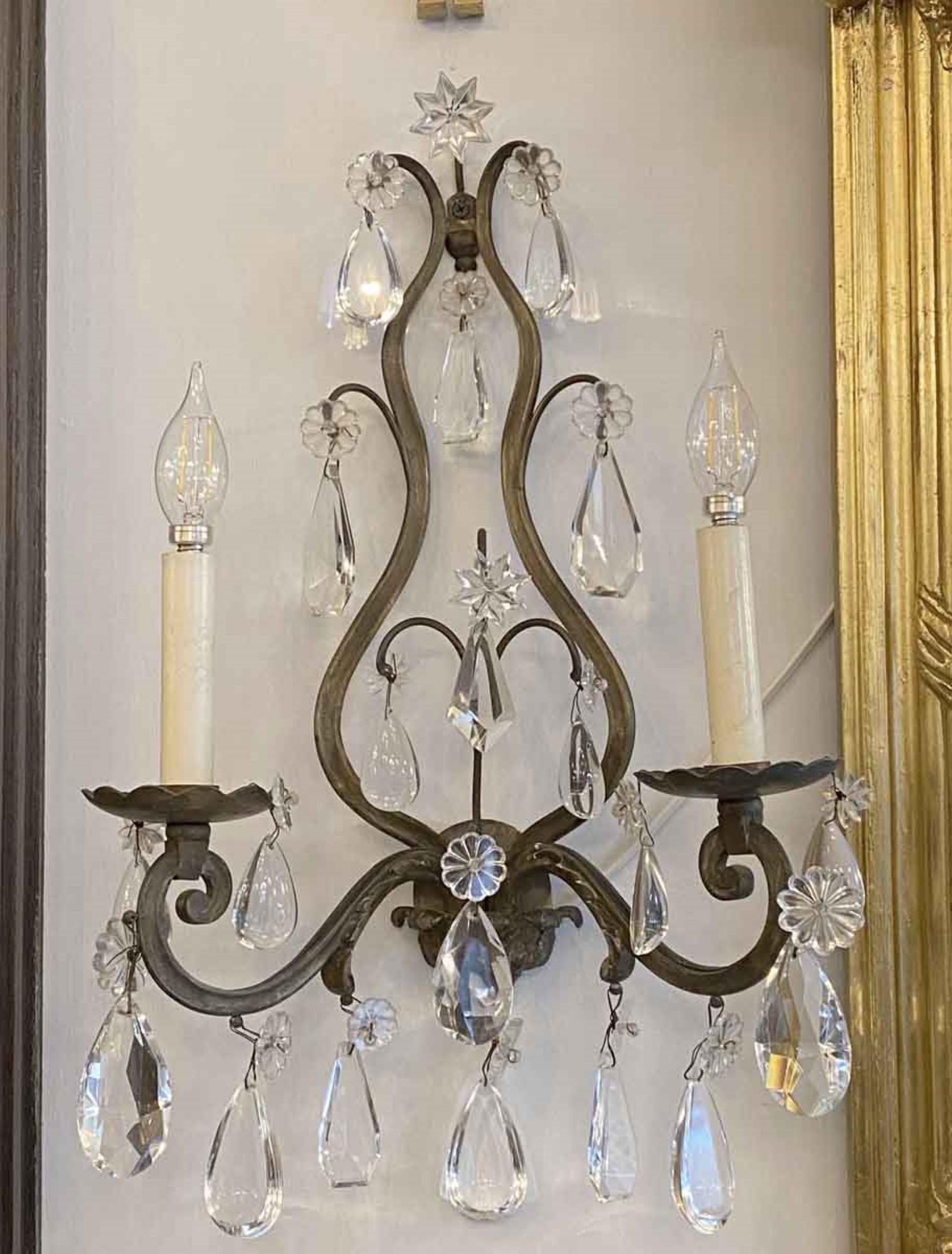 Here is a pair of 1920s French antique wall sconces in bronze and a pleasing assortment of complementary crystals. They each have two lights, and use candelabra bulbs. There are various shaped crystals, of which all have a small flower or star at