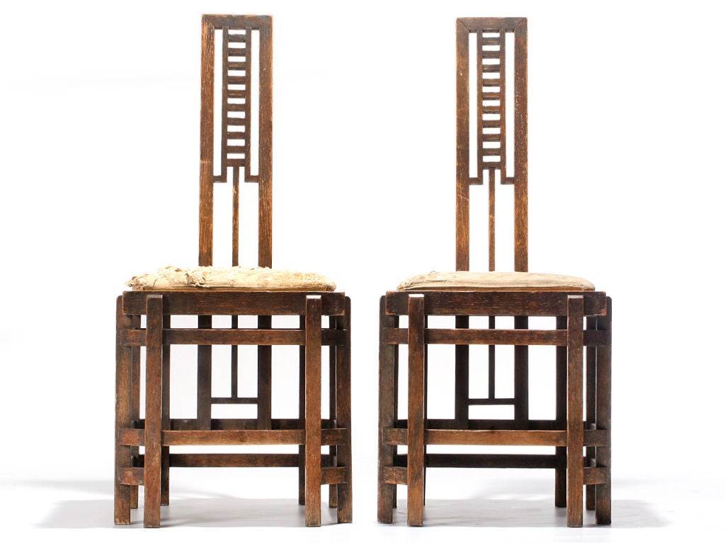 An unusual and highly architectural pair of hall chairs showing both Arts & Crafts and Secessionist influences. These expressive ladder back chairs are crafted of oak and are in excellent original condition. Price includes upholstery fee with