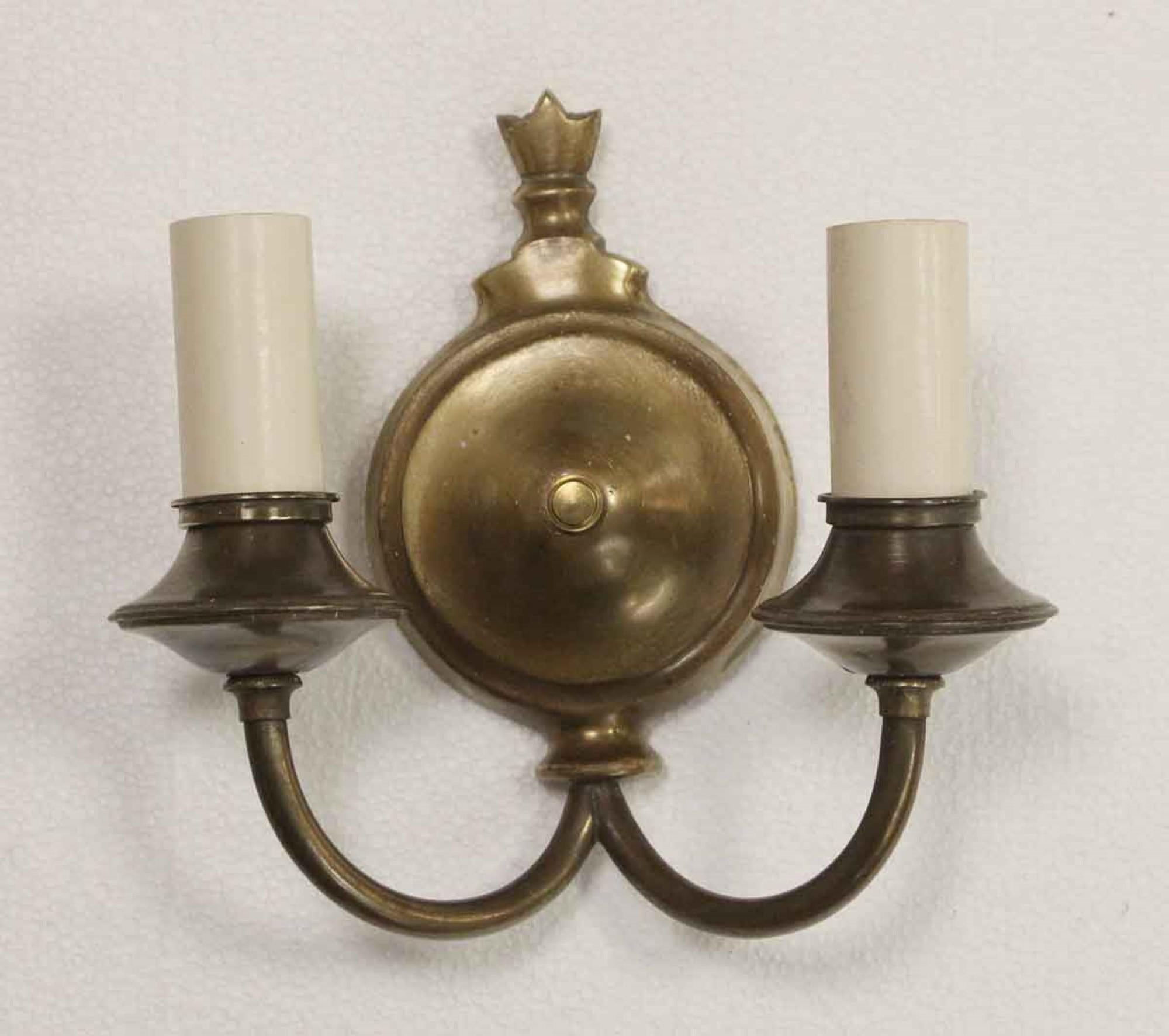 1920s pair of Colonial style two-arm sconces in brass with an antique brass patina with short candlesticks. Small quantity available at time of posting. Priced each. This can be seen at our 400 Gilligan St location in Scranton. PA.
