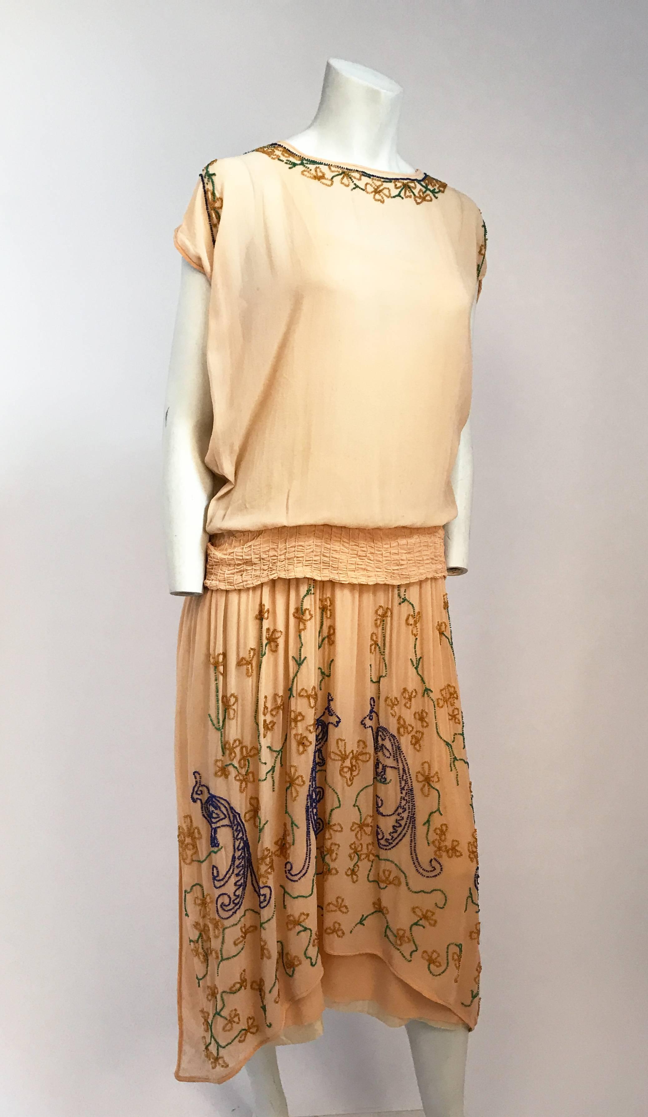 pfirsichfarbenes Glasperlenkleid mit Tropfen-Taille aus den 1920er Jahren. Pfirsichfarbenes Kleid mit tropfenförmiger Taille und mehrfarbigen Glasperlen mit Pfauenmuster. Gesmokter Taillenbund, der im Rücken eine Schleife bildet. Eingebautes Futter