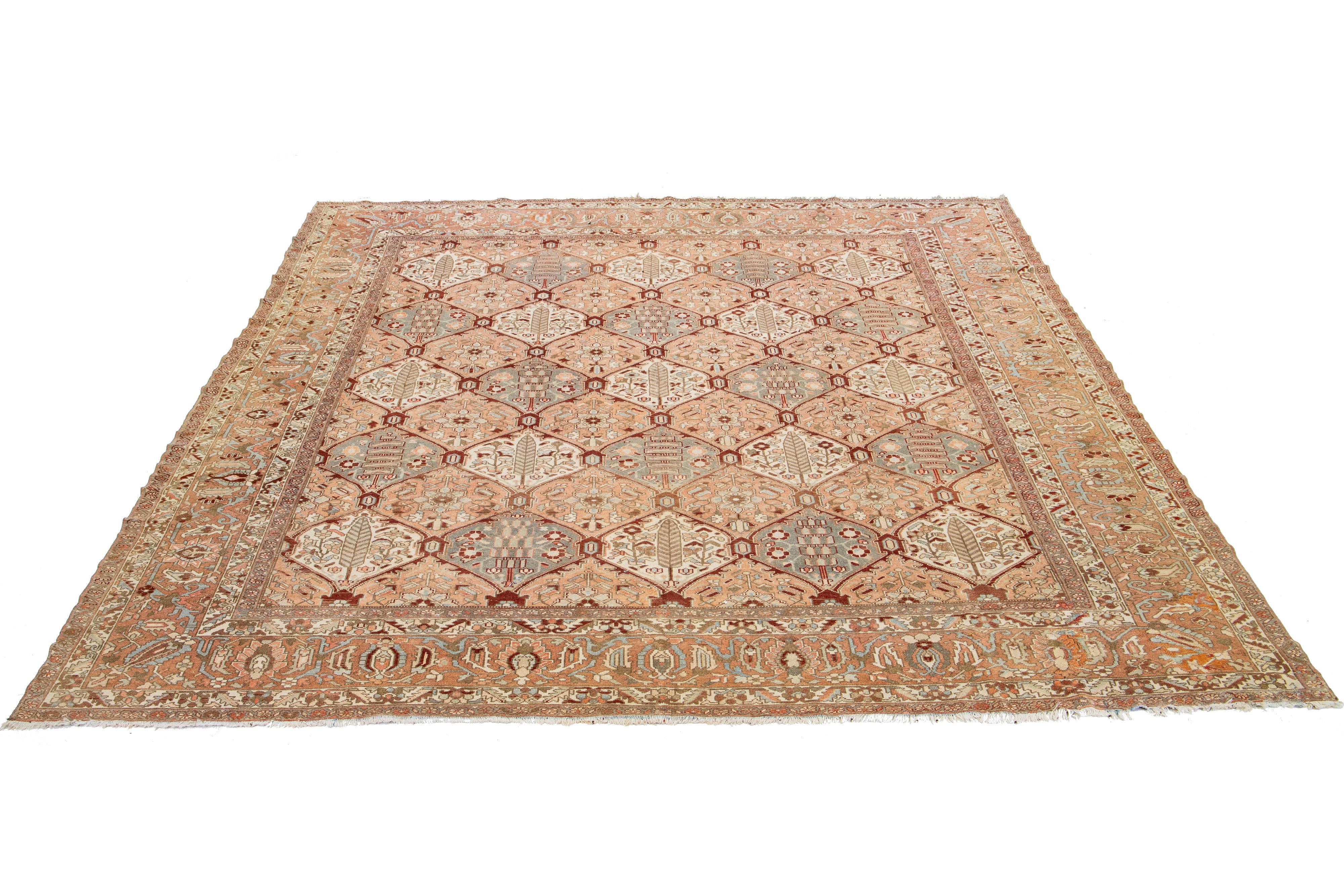 Beautiful Antique Bakhtiari hand-knotted wool rug featuring a peach-colored field. This exquisite Persian rug showcases a classic geometric floral design with blue, beige, red-rust, and gray hues.

This rug measures 12'4