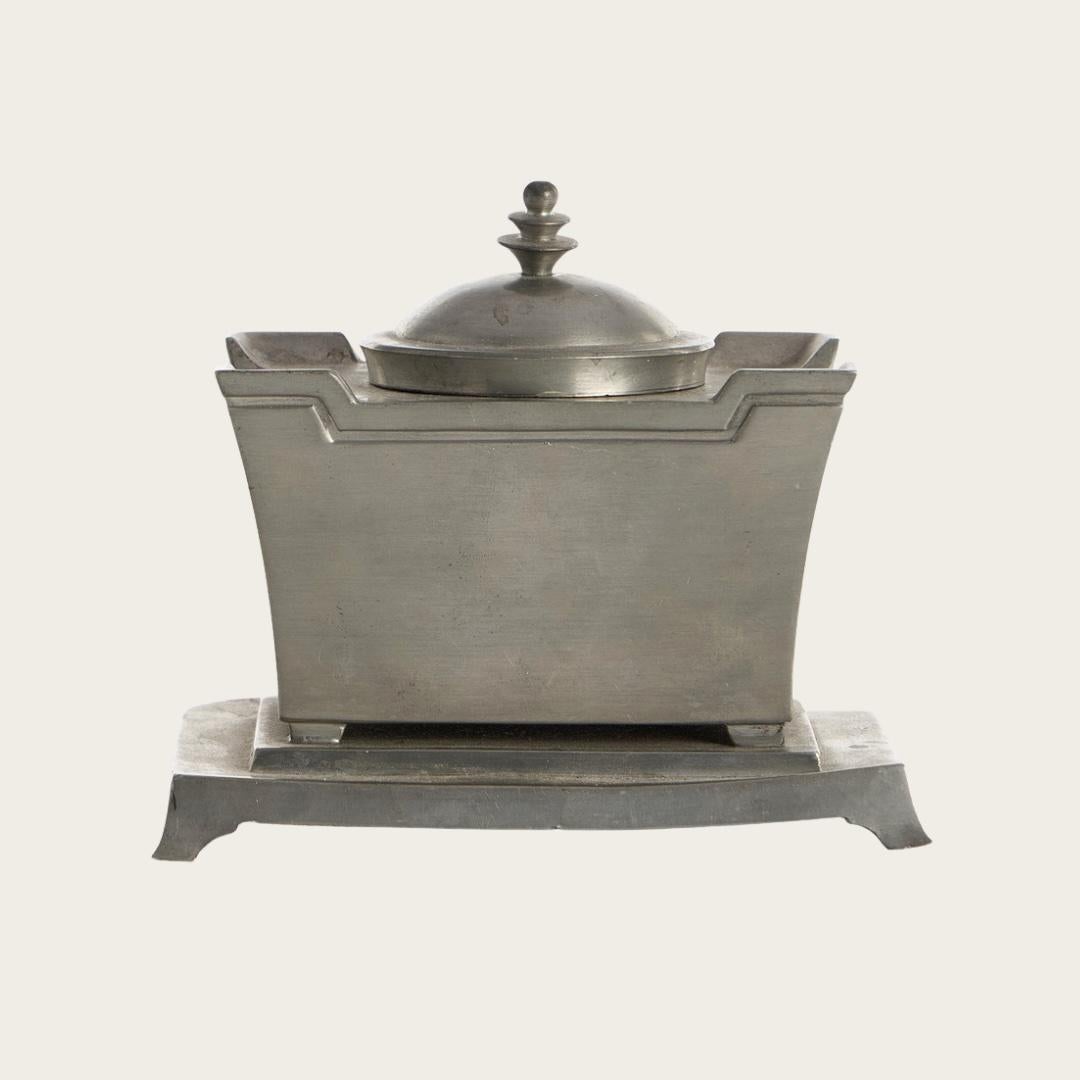 1920s, Denmark. Crafted by Just Andersen, this pewter inkhorn showcases the refined lines of the Swedish Grace movement. The footed base anchors the design while a glass insert provides practical ink storage. Bearing the maker's mark on its