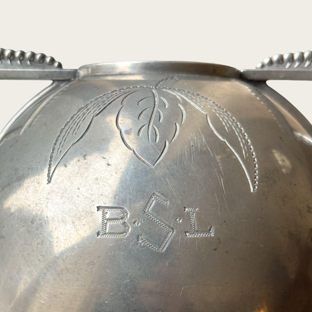 1920s, Sweden. Polished pewter globe vase by Svenskt Tenn with decorative leaf engraving on front and backside and beaded handle details with ribbed vase mouth. Marked by maker on underside. 