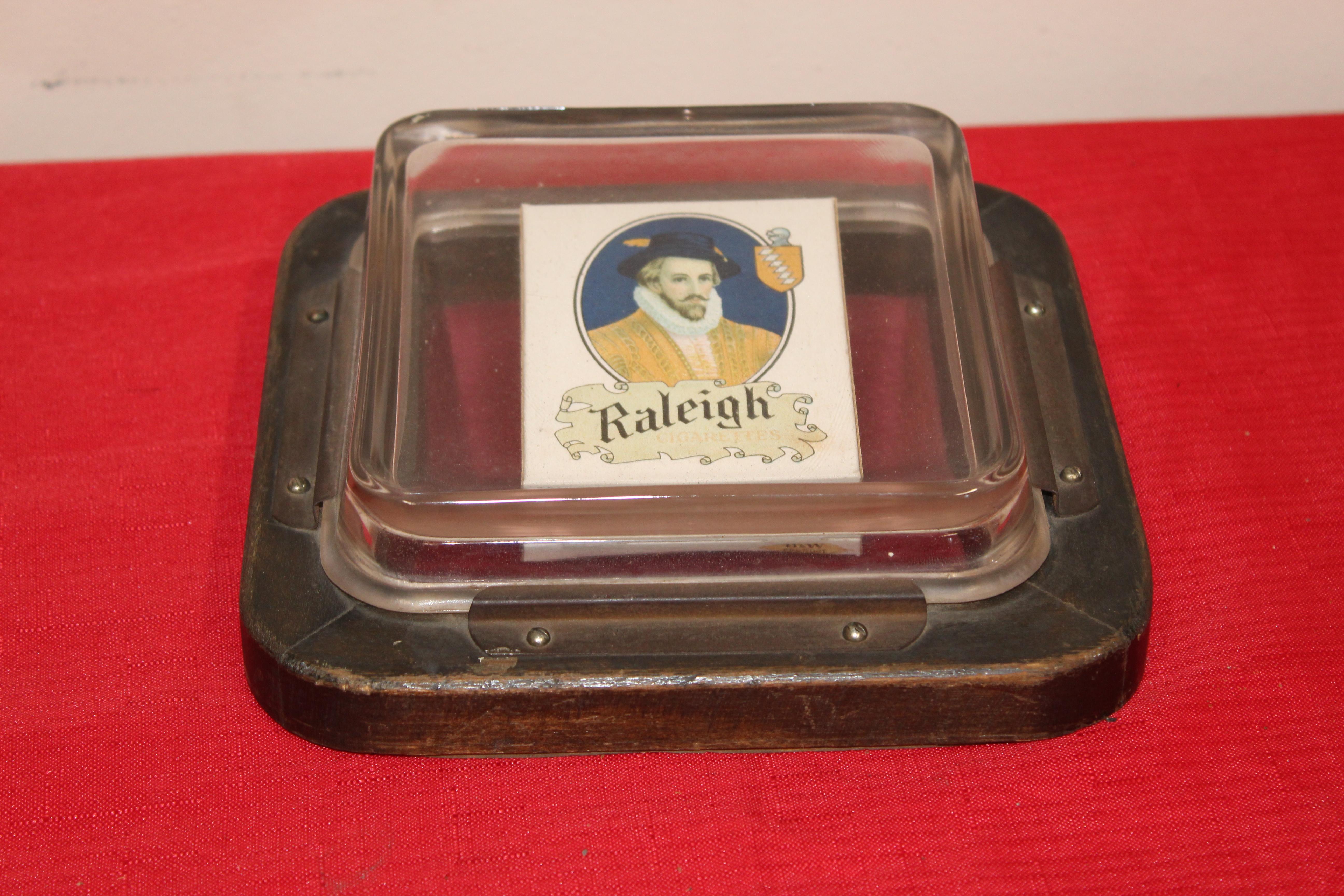 These were used for a variety of things in tobacco shops. Putting customers change in it or sometimes free matches for customers and as always a handy ashtray. Raleigh cigarette pack is stabilized under the glass. Has four brass plates hold the