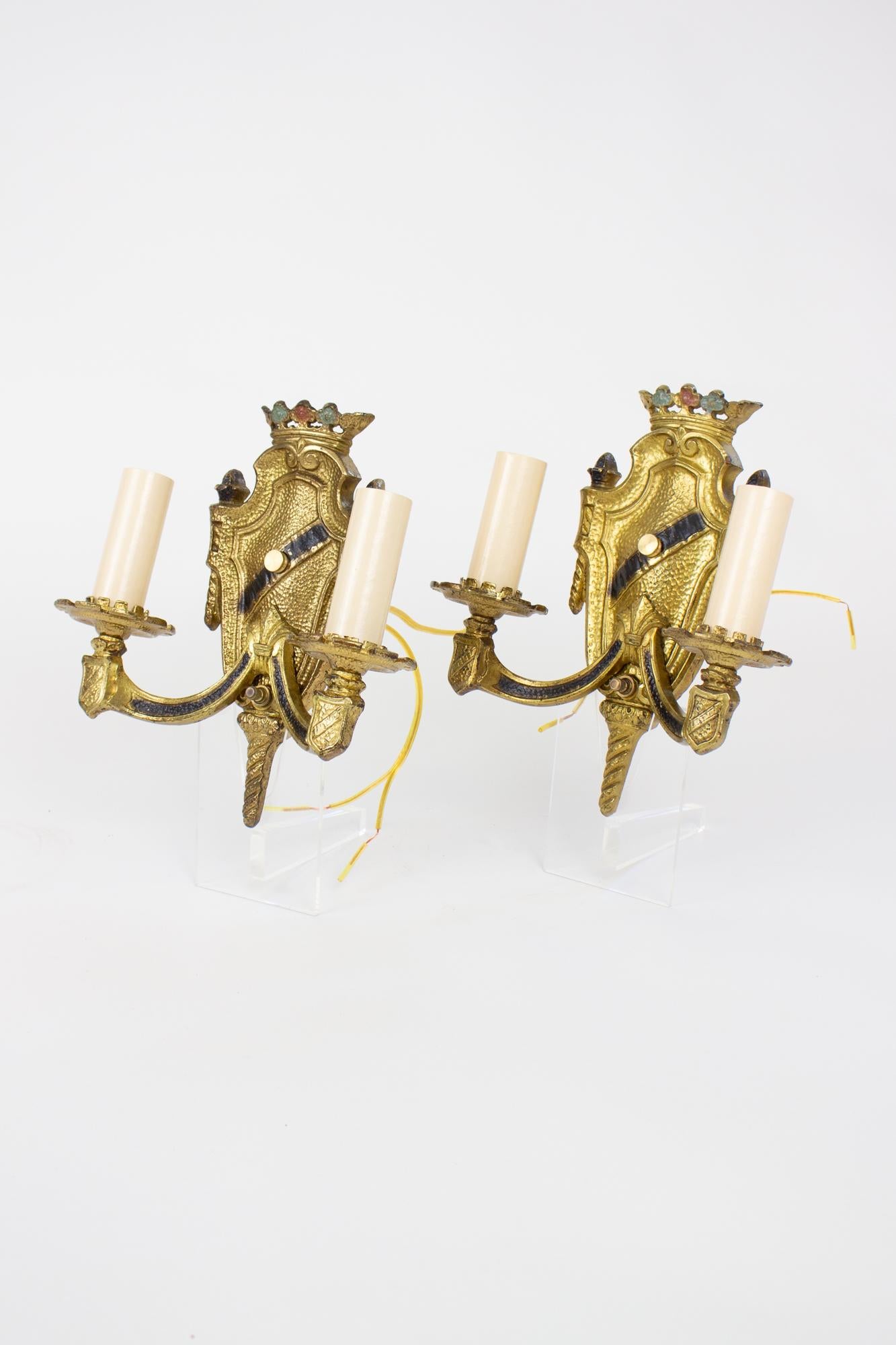 1920’s renaissance revival cast brass sconces, a pair. A lovely pair of shield form double arm sconces in cast brass with original painted polychrome accents. A crown at the top with blue and red accents. The backplate is shieldform with a black