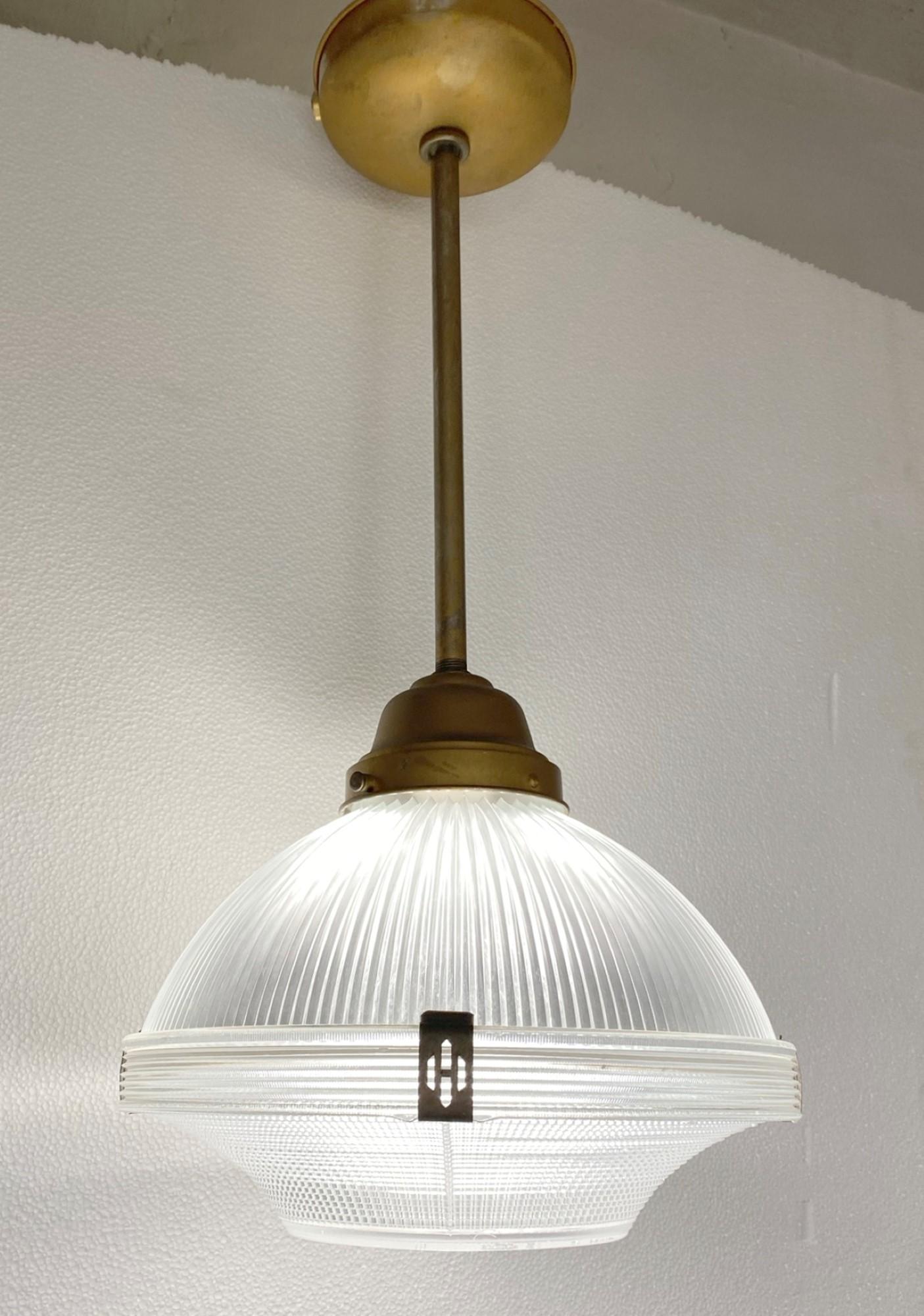 This 1920s prism glass Holophane Industrial pendant light features the original hardware and the original clear prism glass shade. This can be seen at our 2420 Broadway location on the upper west side in Manhattan.