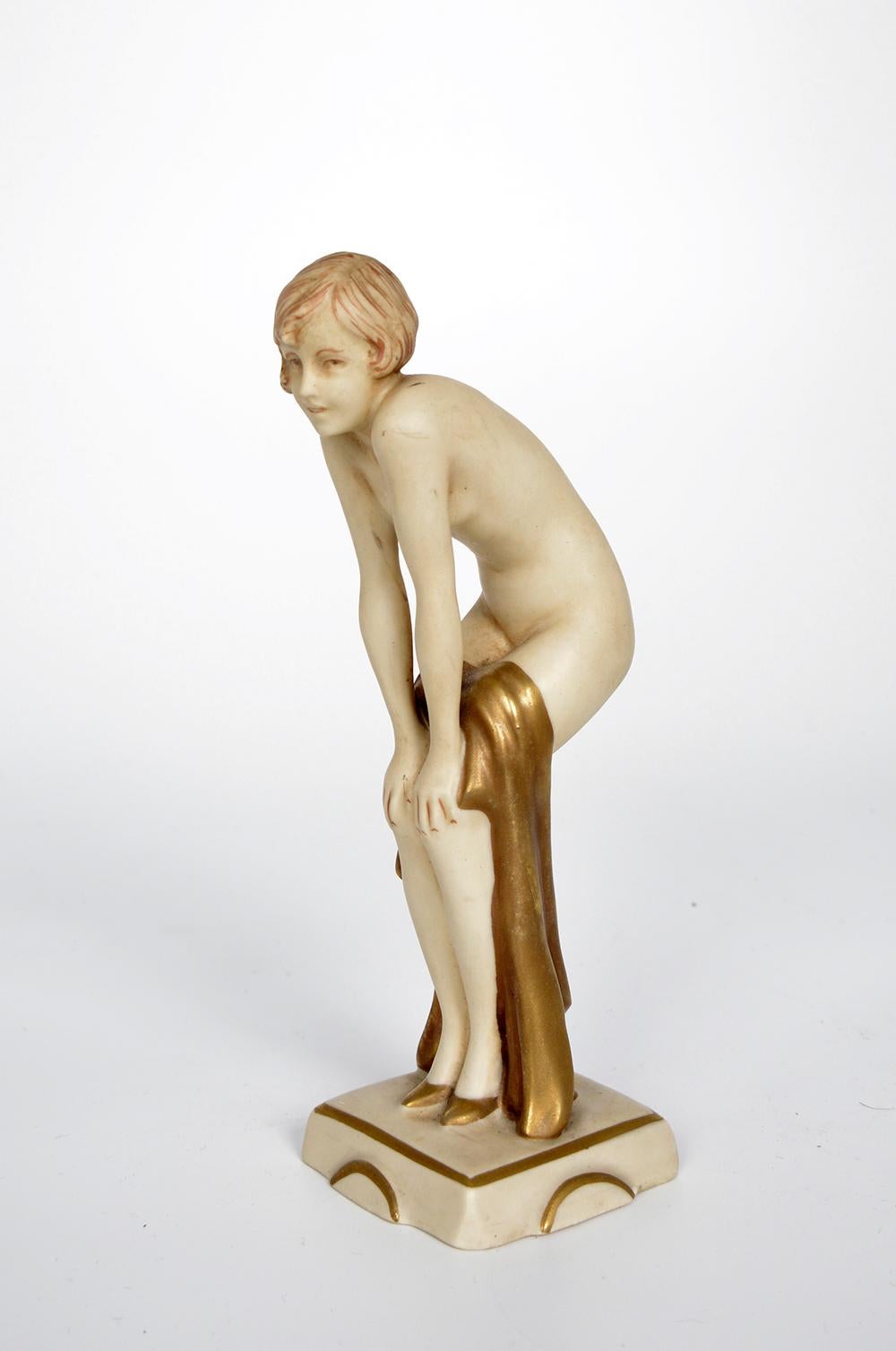 A charming and well-modelled Royal Dux Art Deco figure of a nude female by Elly Strobach (b.1908), with soft bisque ivory flesh tones, beautifully detailed painting of the hair and hands, her knees bent with a gold material draped across her thighs.