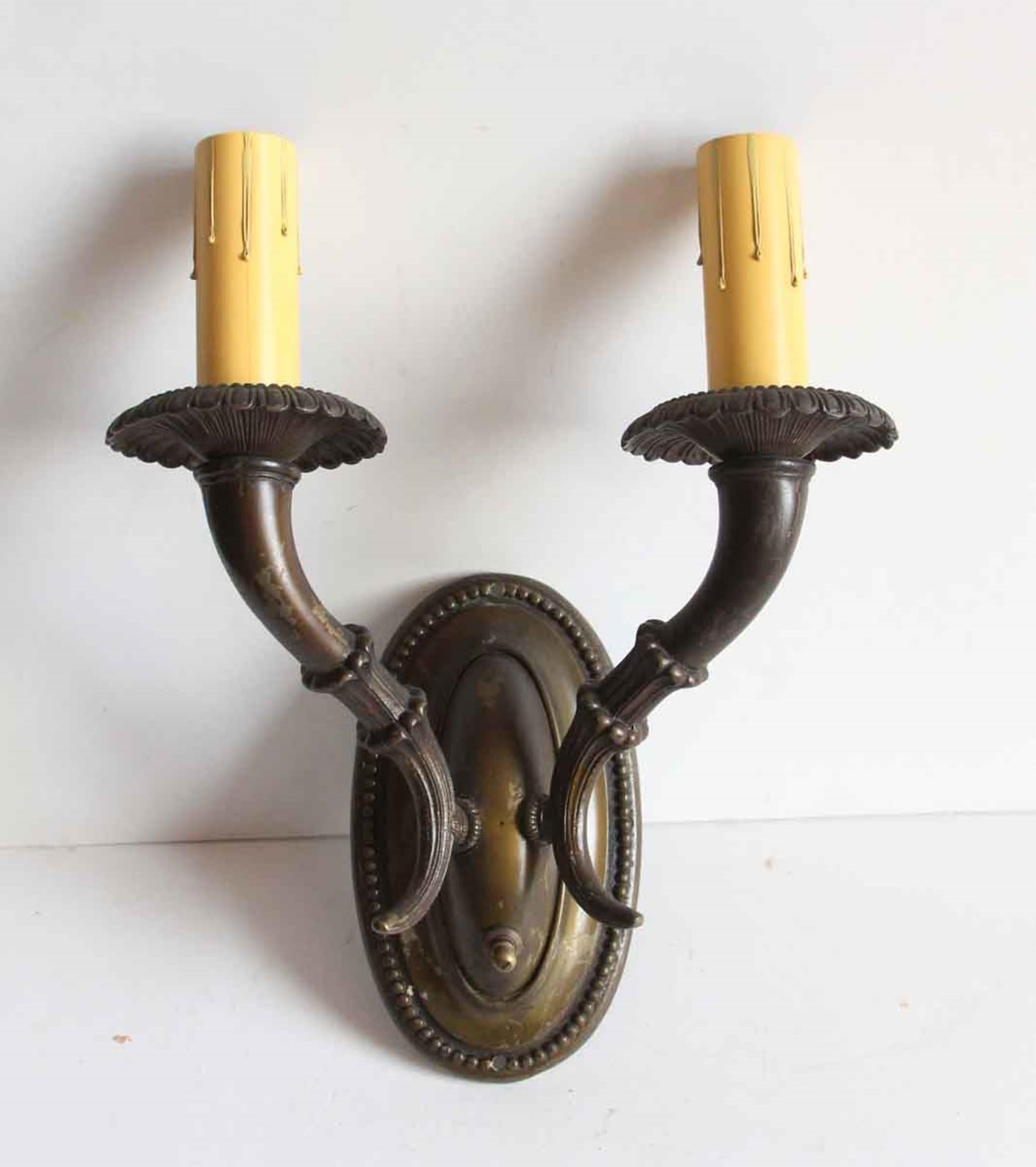 Early 1920s two arm brass candlestick sconces done in an Empire style. Each back is encircled with a beaded detail and each arm is fluted with a cornucopia-like horn coming up to light socket. Price includes restoration. This can be seen at our 400