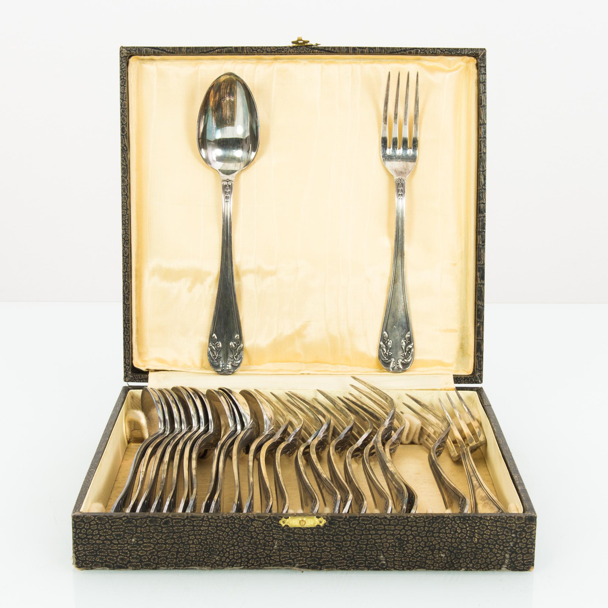 A set of silver-plated cutlery from Europe, circa 1920. Silver forks and spoons rest within a square box, which closes with a delicate gold clasp. The box is finished in dark brown snakeskin, while the inside is lined with pale gold silk. The form