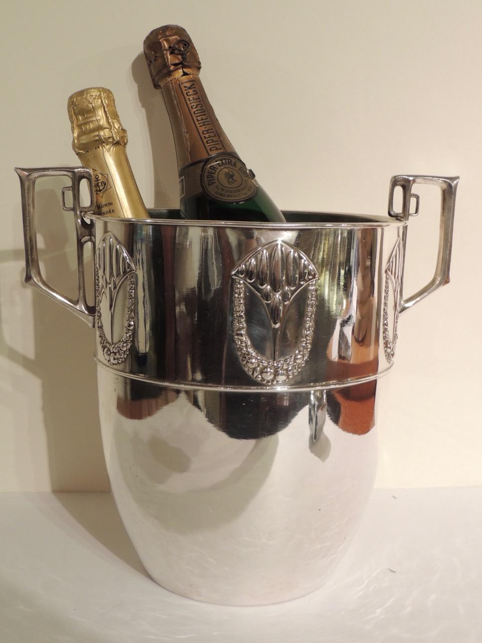 A 1920s sliver champagne cooler with lovely “repousse” embellishment of a cascading wreath of flowers. The handles have a geometric “Jugendstil” design. Repousse is a technique in which there is an embossed design, pressed or hammered into relief