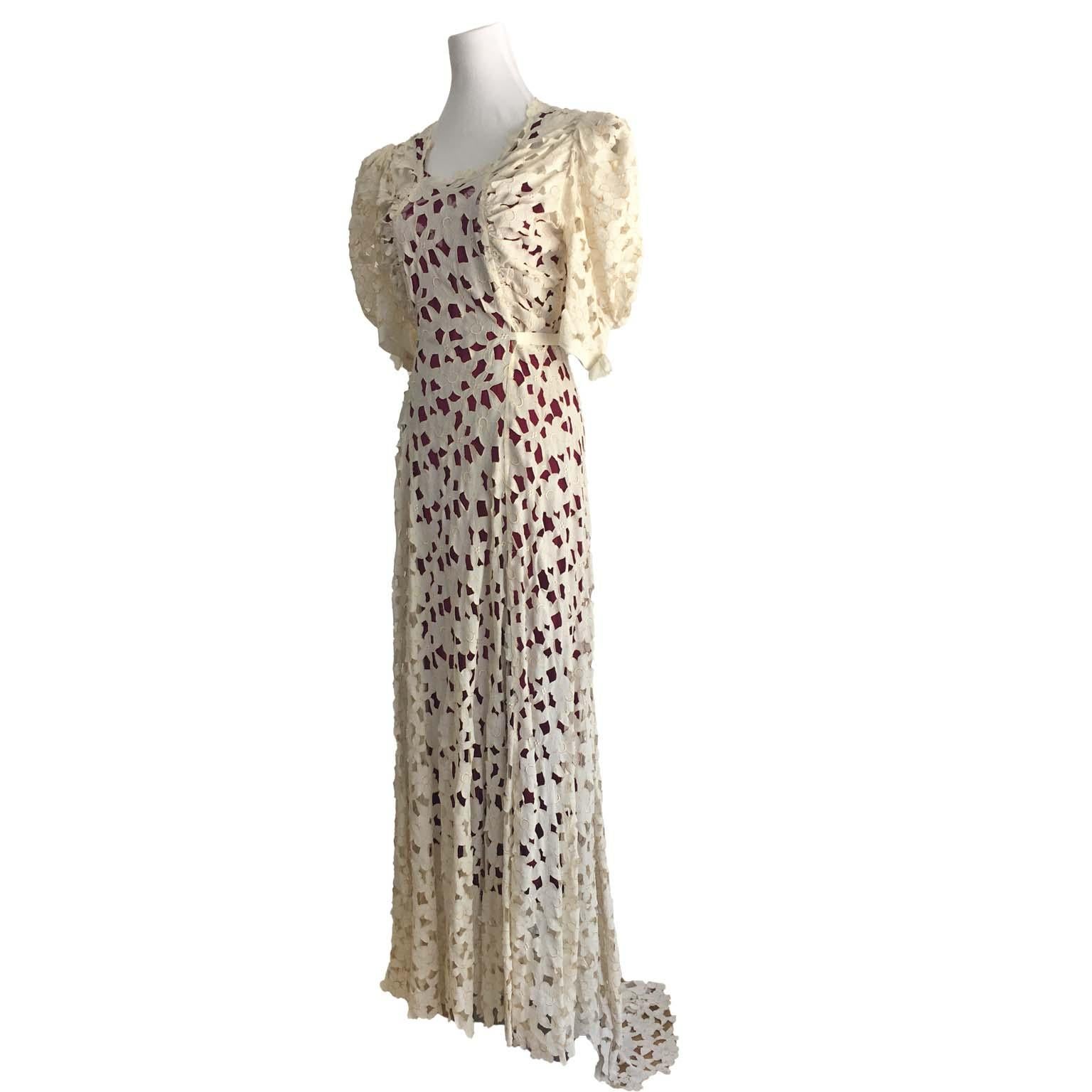 Elegant circa 1920s white cream cutout lace dress. 
Ivory Off white lace is layered over a bordeaux under lining with incredible contrast. 
The dress has full length light puff sleeves. The seamed waist skirt is A line to a semi train skirt. The