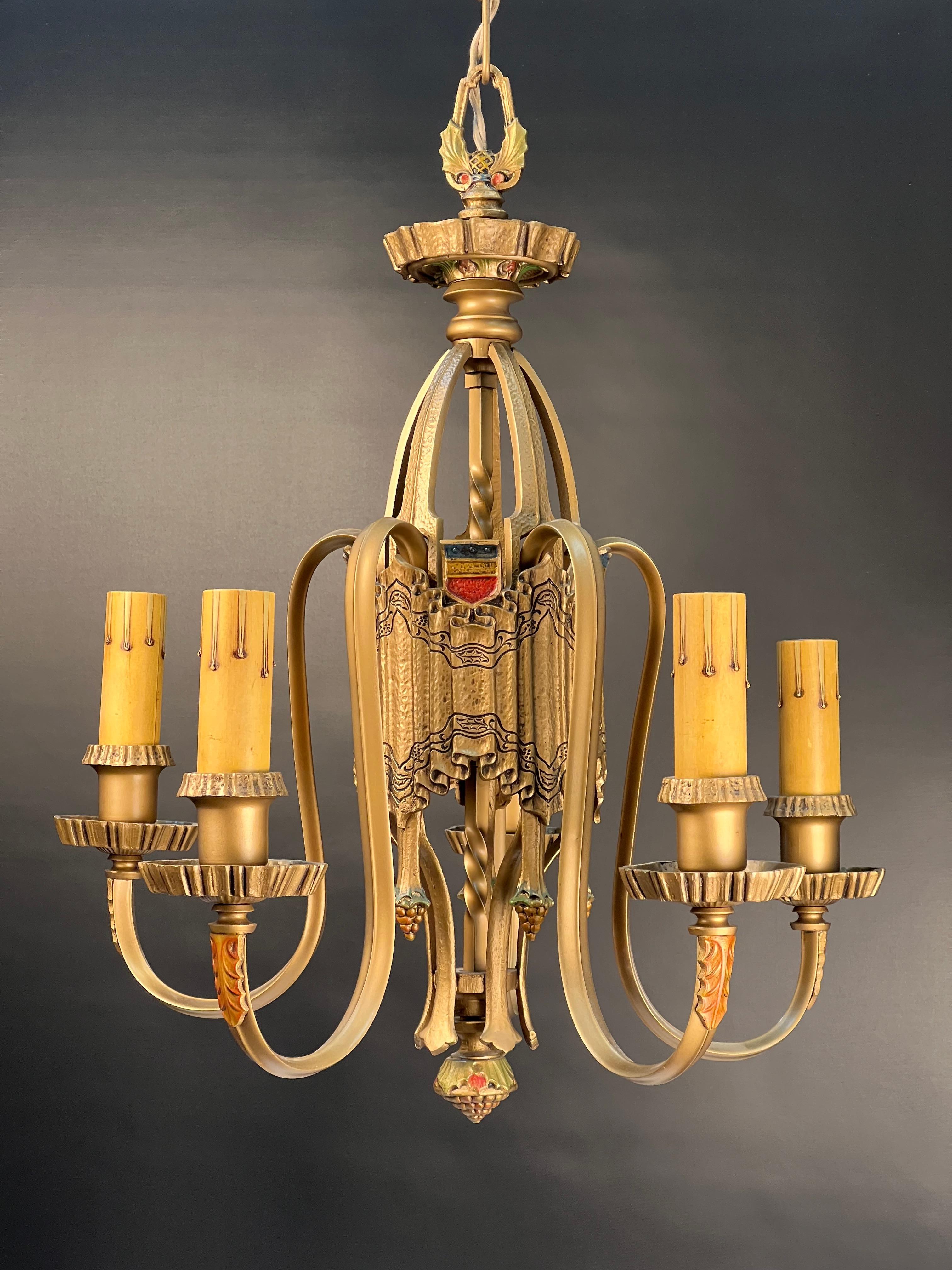 A handsome 1920's Tudor revival five light chandelier with a subtly rich gold patina with classic polychrome highlights.
The central body of this chandelier is cast in the classical design of a linen fold. Linen fold started as carved wood imitating