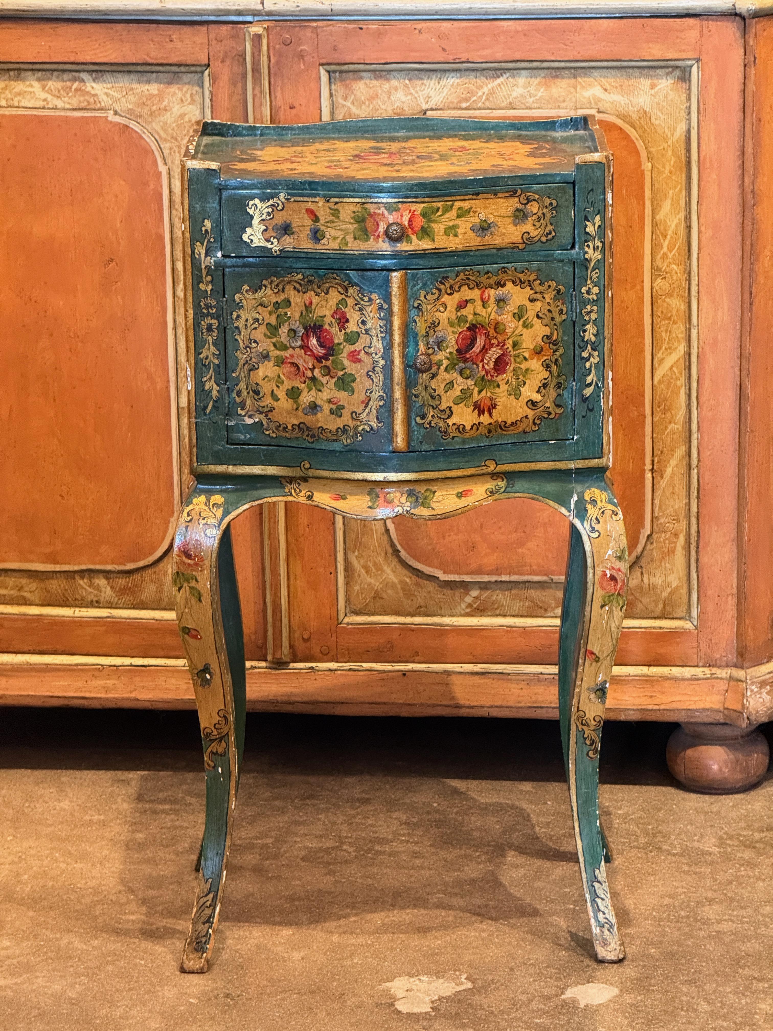 Tavolino veneziano delicatamente dipinto con decorazioni floreali e a volute su una forma sagomata e smerlata. Presenta un cassetto singolo sopra le ante a pannelli, il tutto sollevato su gambe cabriole. Finitura originale verniciata con colori