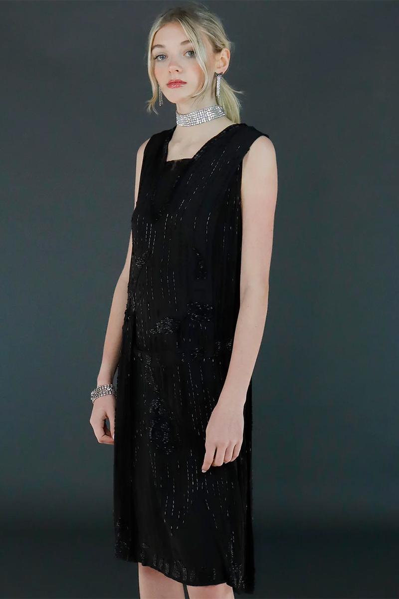 This lovely vintage 1920's black silk crepe flapper dress features glistening iridescent black bugle beads that form vertical lines down the dress and a beautiful floral pattern on the front of the skirt. The neckline is heavily covered with triple