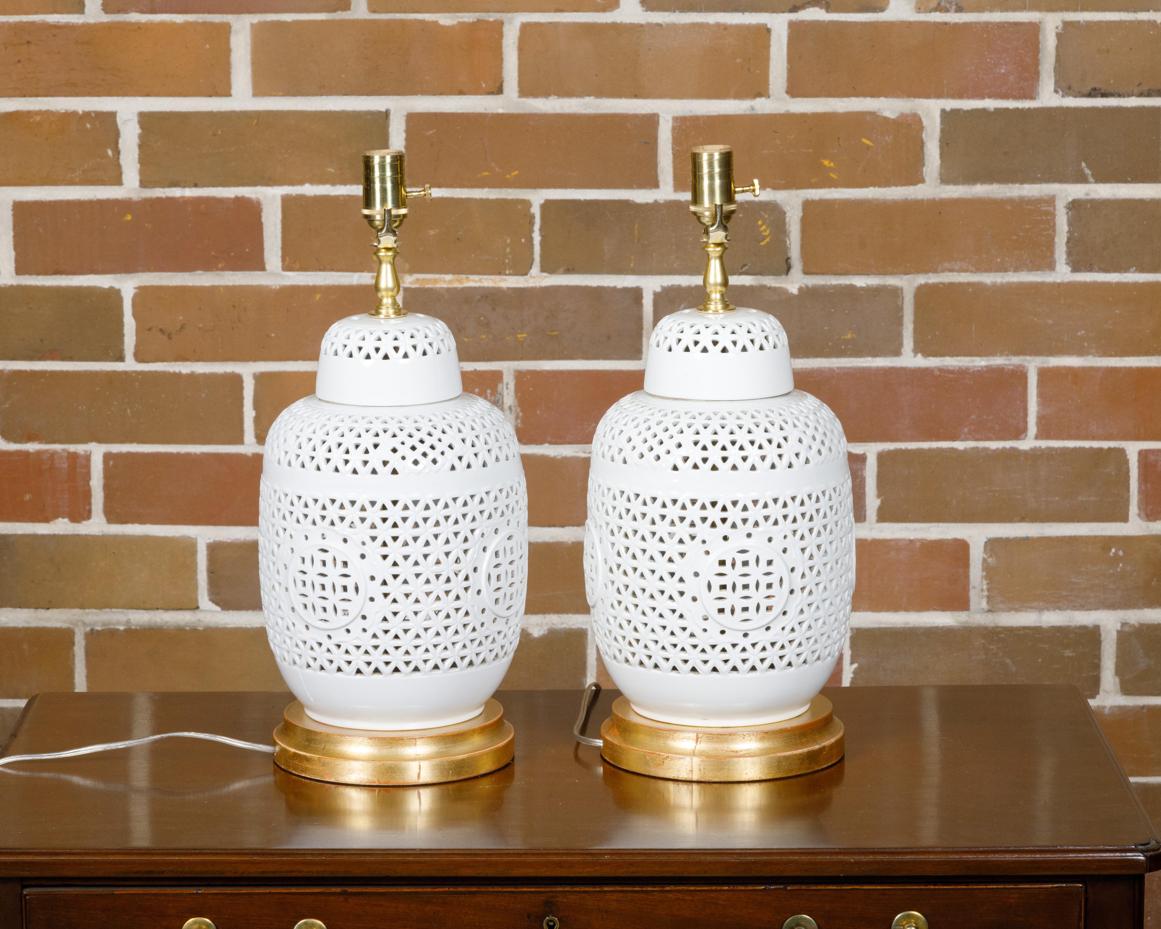 Paire de vases en porcelaine blanche à décor géométrique percé, datant de 1920 environ, transformés en lampes de table câblées pour les États-Unis et montés sur des bases circulaires en bois doré. Whiting par son élégante simplicité, cette paire de