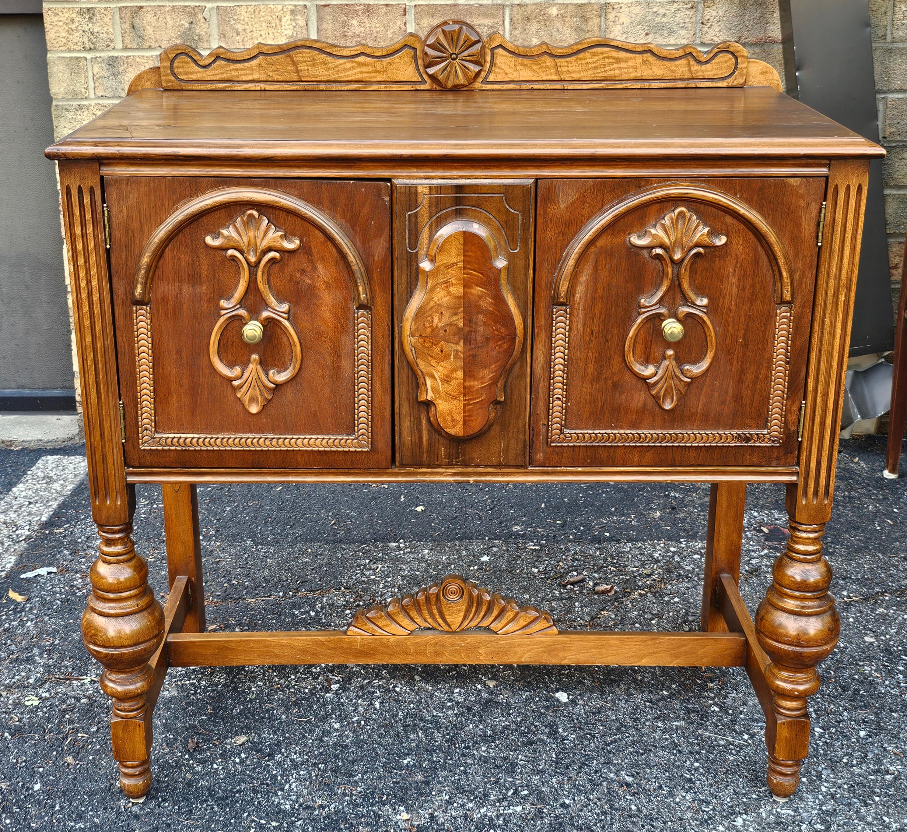 A 1920s William and Mary Tudor-style walnut server or buffet, featuring carved details, original hardware, and a restored finish. These pieces were typically made in America and often included solid oak construction with dovetailed drawers. The