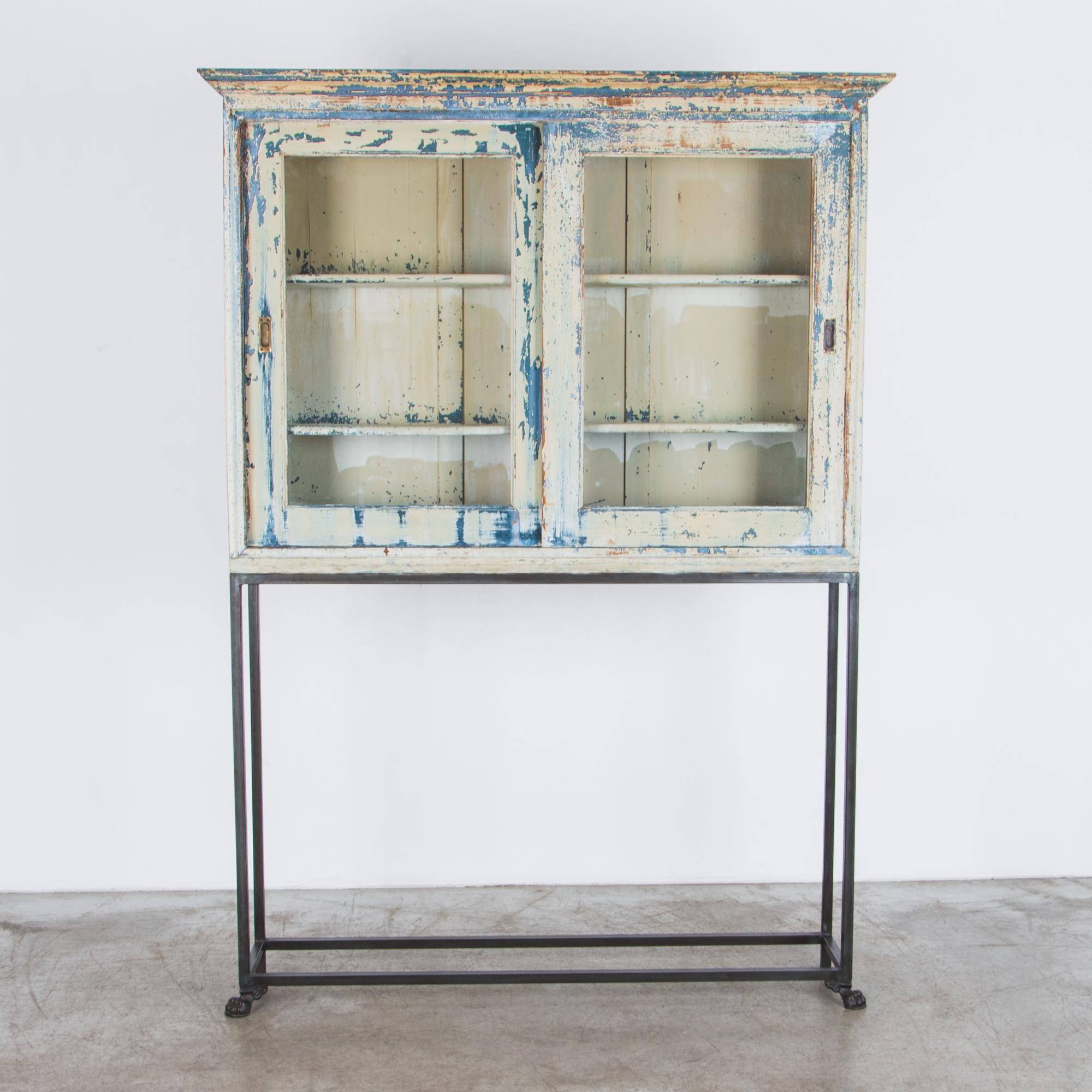 This wooden vitrine features two shelves and a set of glass-fronted sliding doors, made in France in 1920. A charming patina reveals layers of cornflower blue, ochre and a cream white. The piece has been refreshed in our atelier and fitted with a