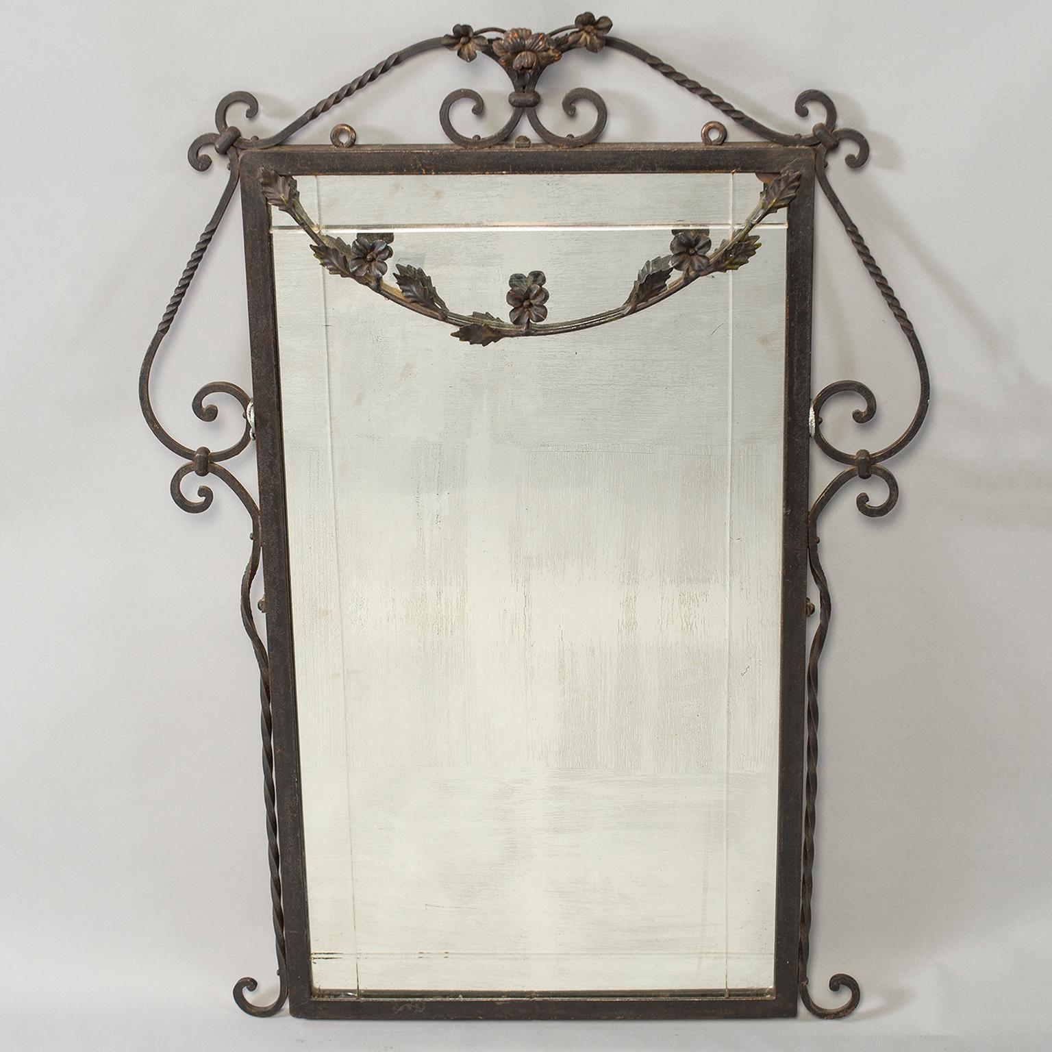 Mirror has a hand-wrought iron frame with a floral crest and decorative swag, circa 1920s. Scrolled details at the base and top with an iron chain for hanging.