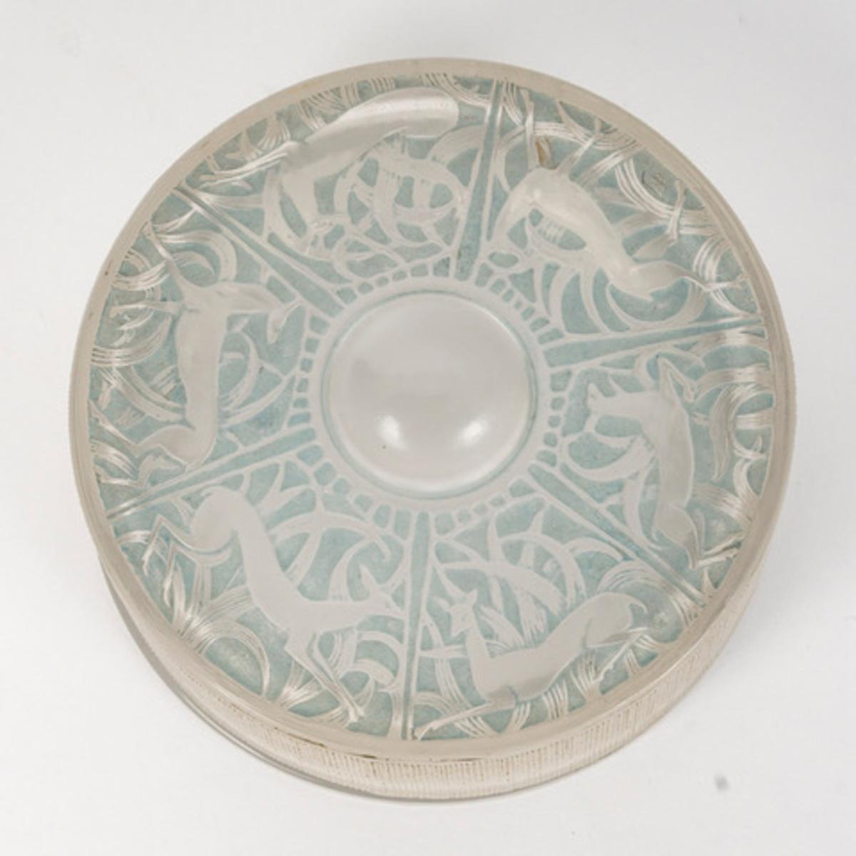 Molded pressed white glass box with a polished glass base and satin glass lid decorated with deer, enhanced with a light blue patina.

Signature molded on the edge.
Model created in 1924 and discontinued in 1937.

Diameter: 8.5 cm 

 Bibliography: