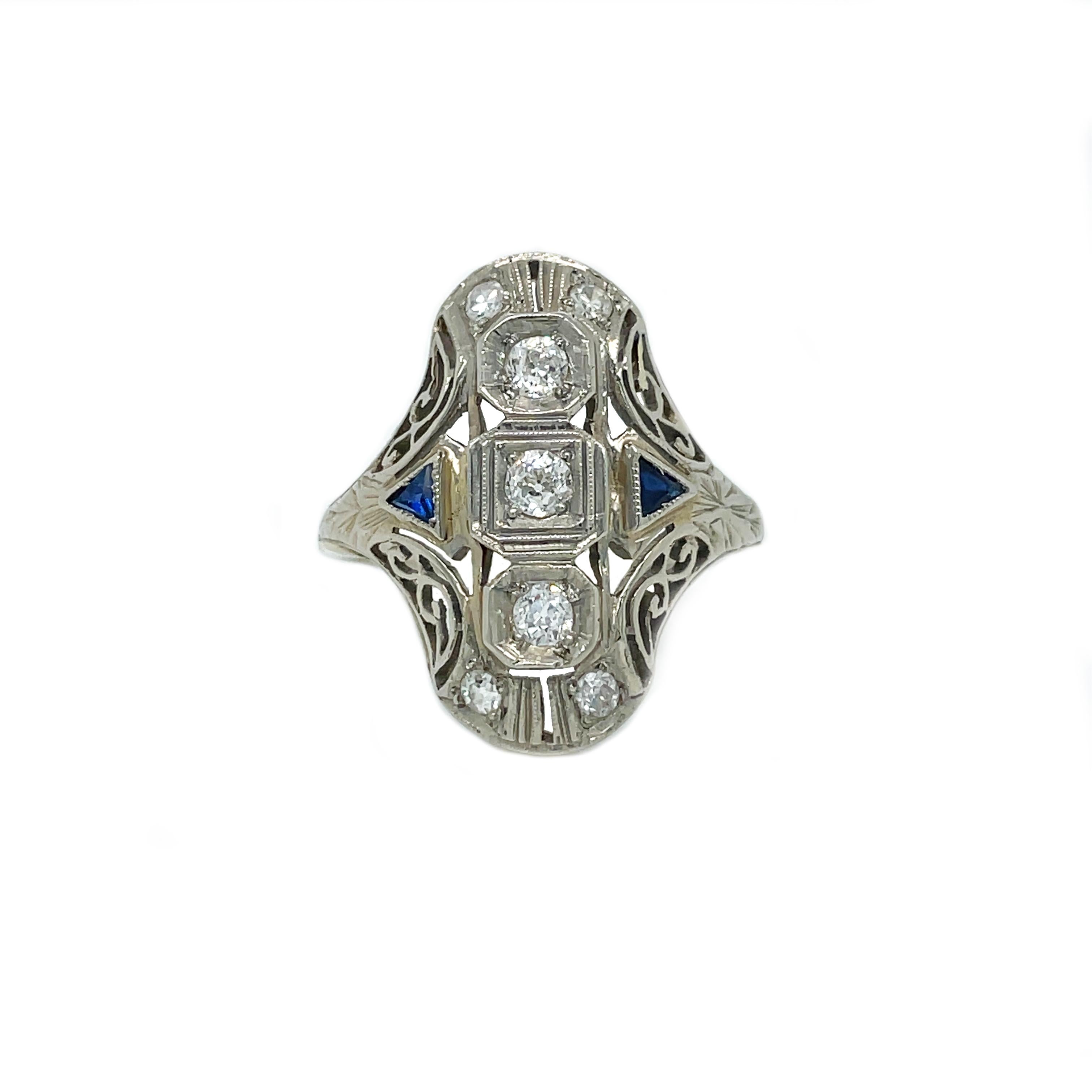 This is a stunning Art Deco ring showcasing 7 gorgeous sparkling diamonds and lovely white gold filigree! This is a gorgeous example of 1920s Deco jewelry in amazing condition. The ring features a sparkling trio at its center of white round diamonds