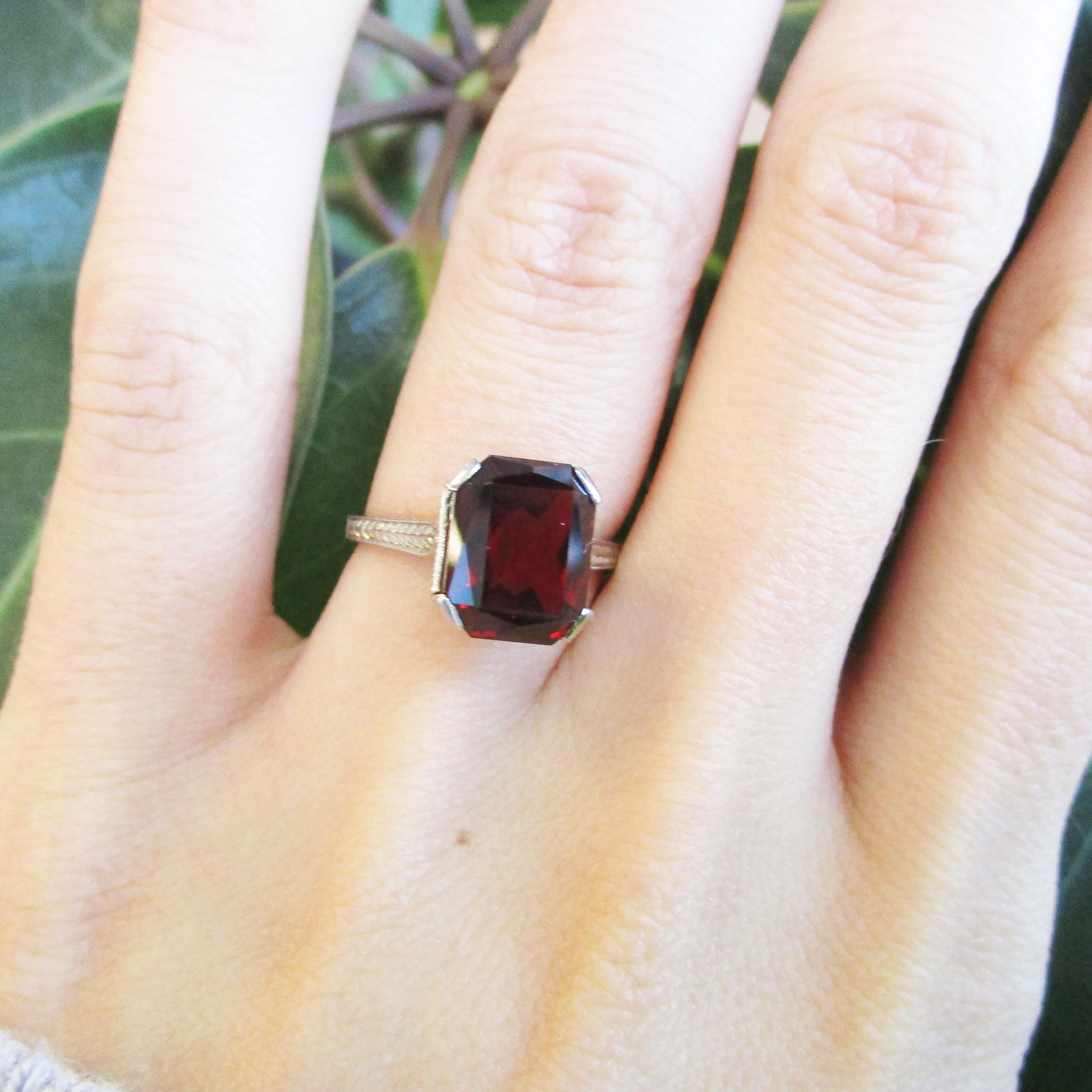 This is an absolutely arresting Art Deco ring from 1925 in 18k white gold with a truly breathtaking red garnet center stone. The delicate ring features finely engraved detailing on the shoulders and under-gallery that creates a subtle layer of