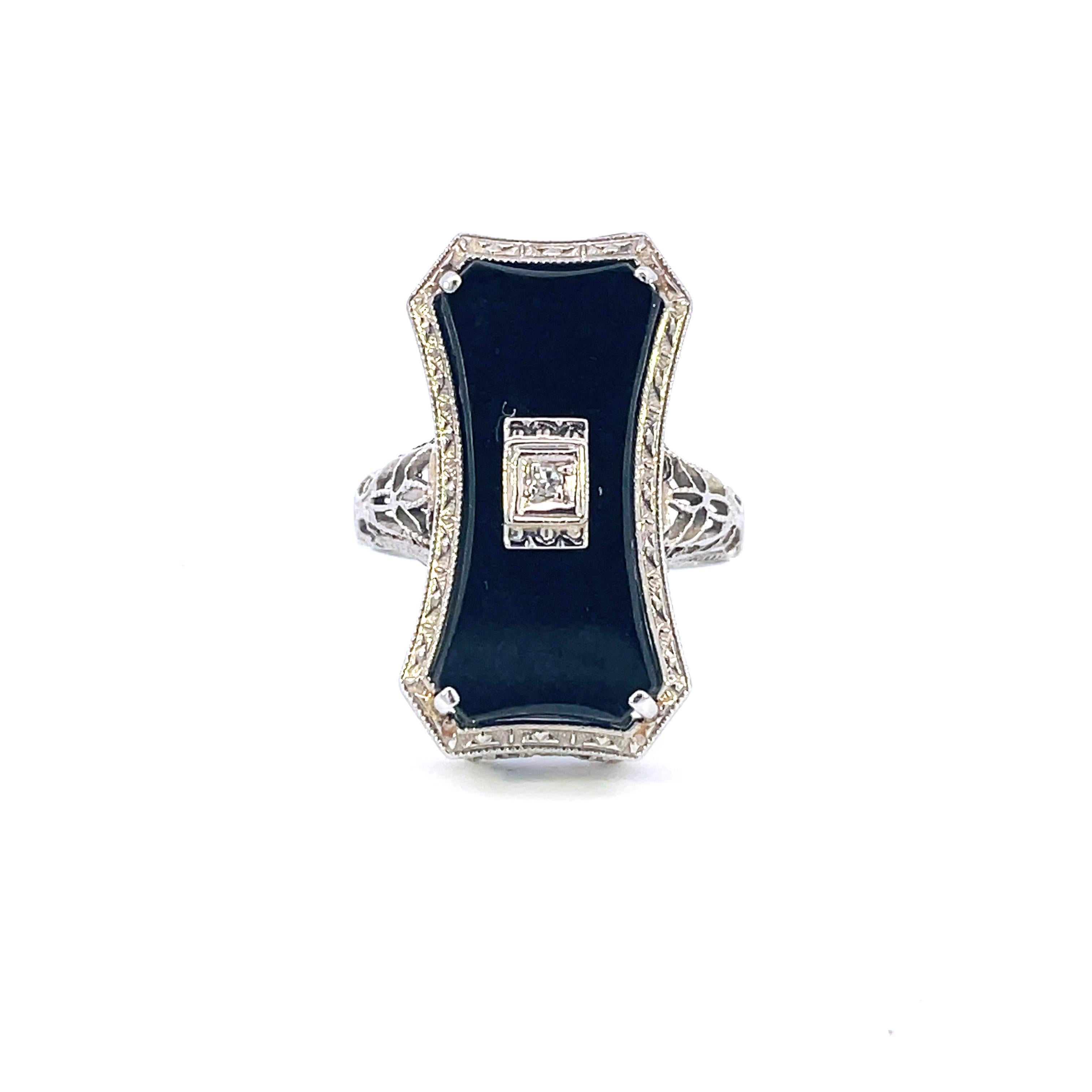 This is a unique Art Deco ring crafted in 14K white gold that showcases a beautiful Black Jade tablet adorned with a white diamond at the center. Delightfully Deco, the ring has marvelous and fanciful filigree along the shoulders and framing the