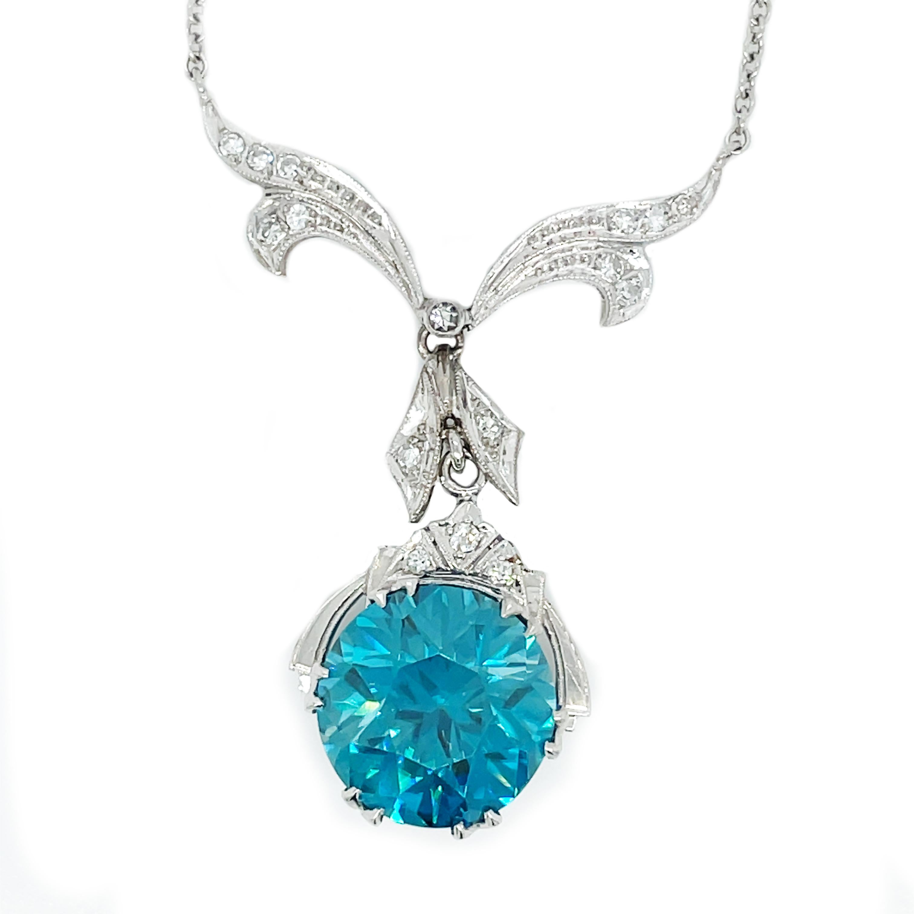 Diese Art Deco-Halskette besticht durch einen spektakulären blauen Zirkon, der mit einer wunderschönen diamantbesetzten Schleife aus Platin verbunden ist! Dieses bezaubernde Schmuckstück wird Sie umhauen! Ein wunderschöner und beeindruckender runder