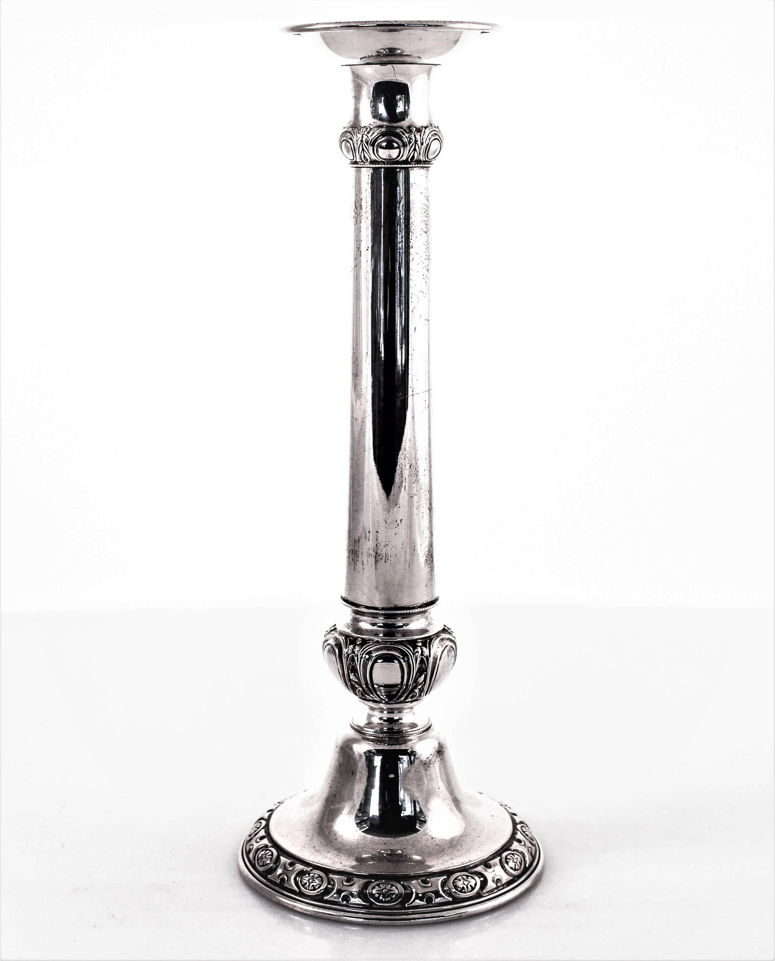 These Art Deco candlesticks have a columnar shape with a decorative motif around the bottom, waist and neck. Around the bottom an oval shaped pattern is interspersed between an H-like design. Around the waist and neck a similar design; complimenting