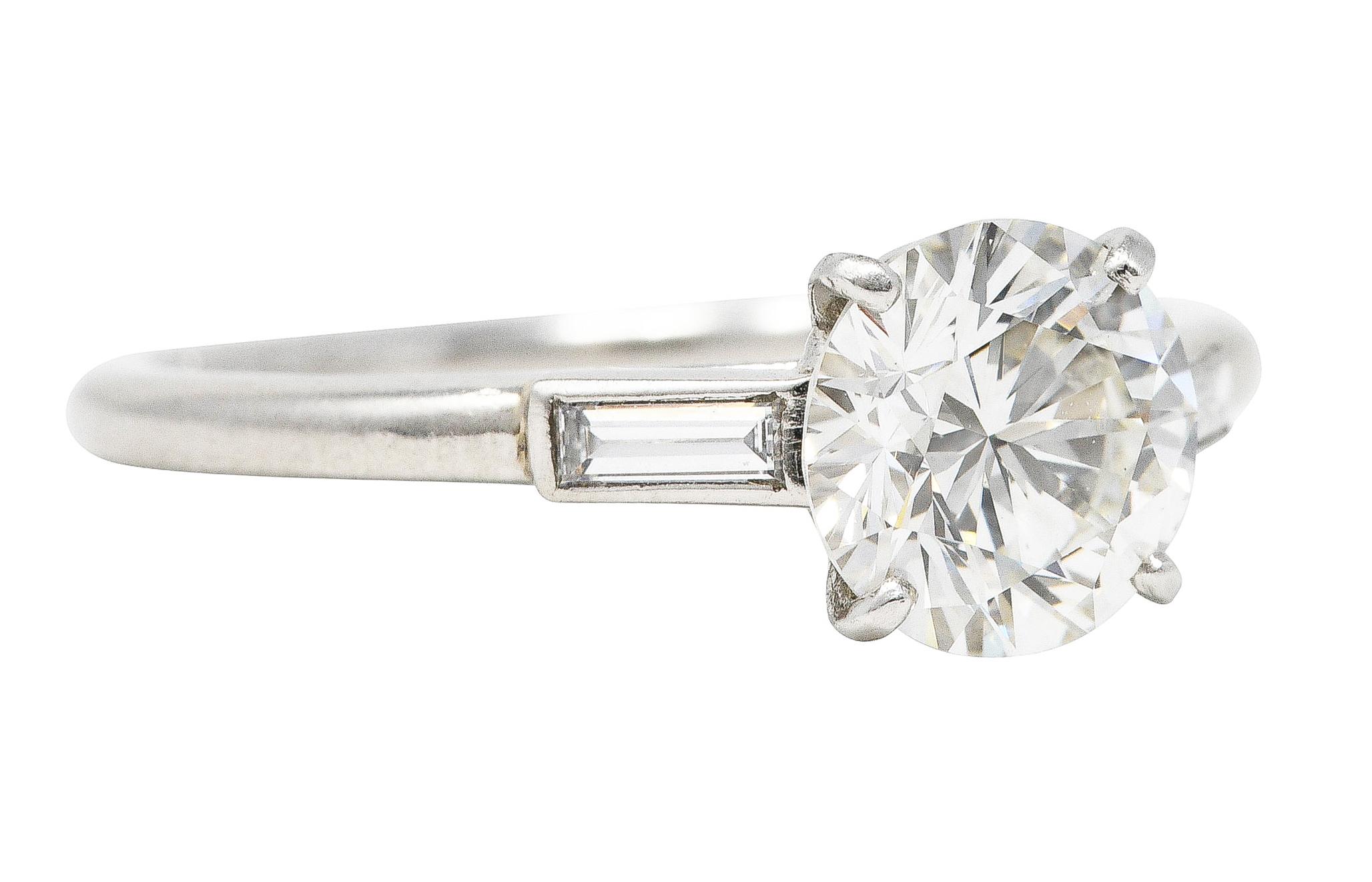 Featuring a round brilliant cut diamond weighing 1.33 carat - H color with VS2 clarity. Set in a tapered basket and flanked by cathedral shoulders. Flush set with straight baguette cut diamonds weighing in total approximately 0.15 carat - matched to