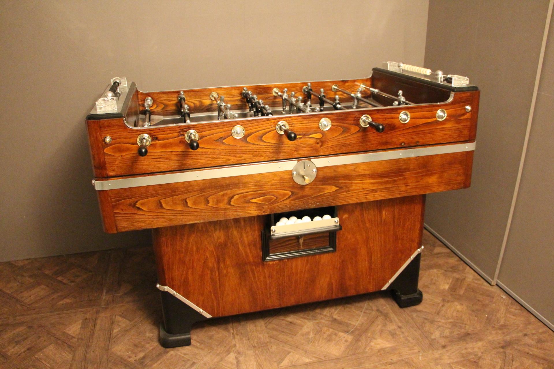 This foosball table features a honey color walnut. It still has got its four original ashtrays by Lalique, as well as all its polished aluminium pieces. Its players are made of turned wood and its field is green. It is coin operated.
Its shape is