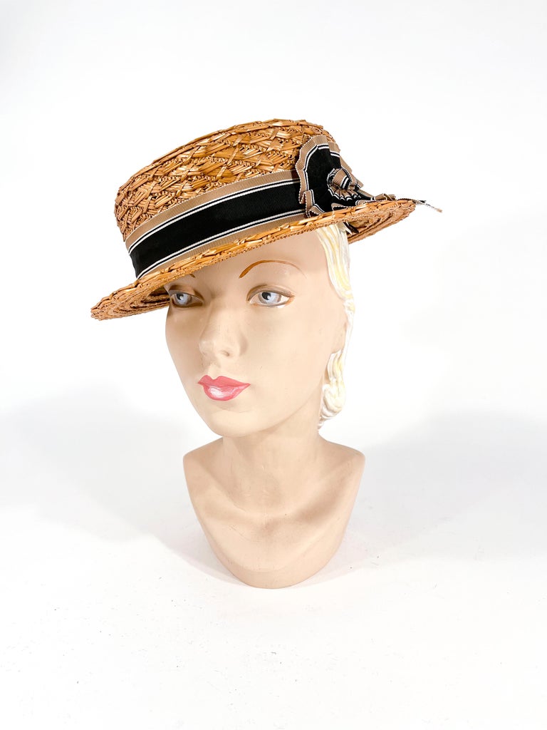 Late 1930s to Early 1940s woman woven straw boater hat finished with a tricolored stripped grosgrain ribbon and a hand-made coward decoration. The interior is unlined and has an attached elastic band that is worn in the back of the head under the