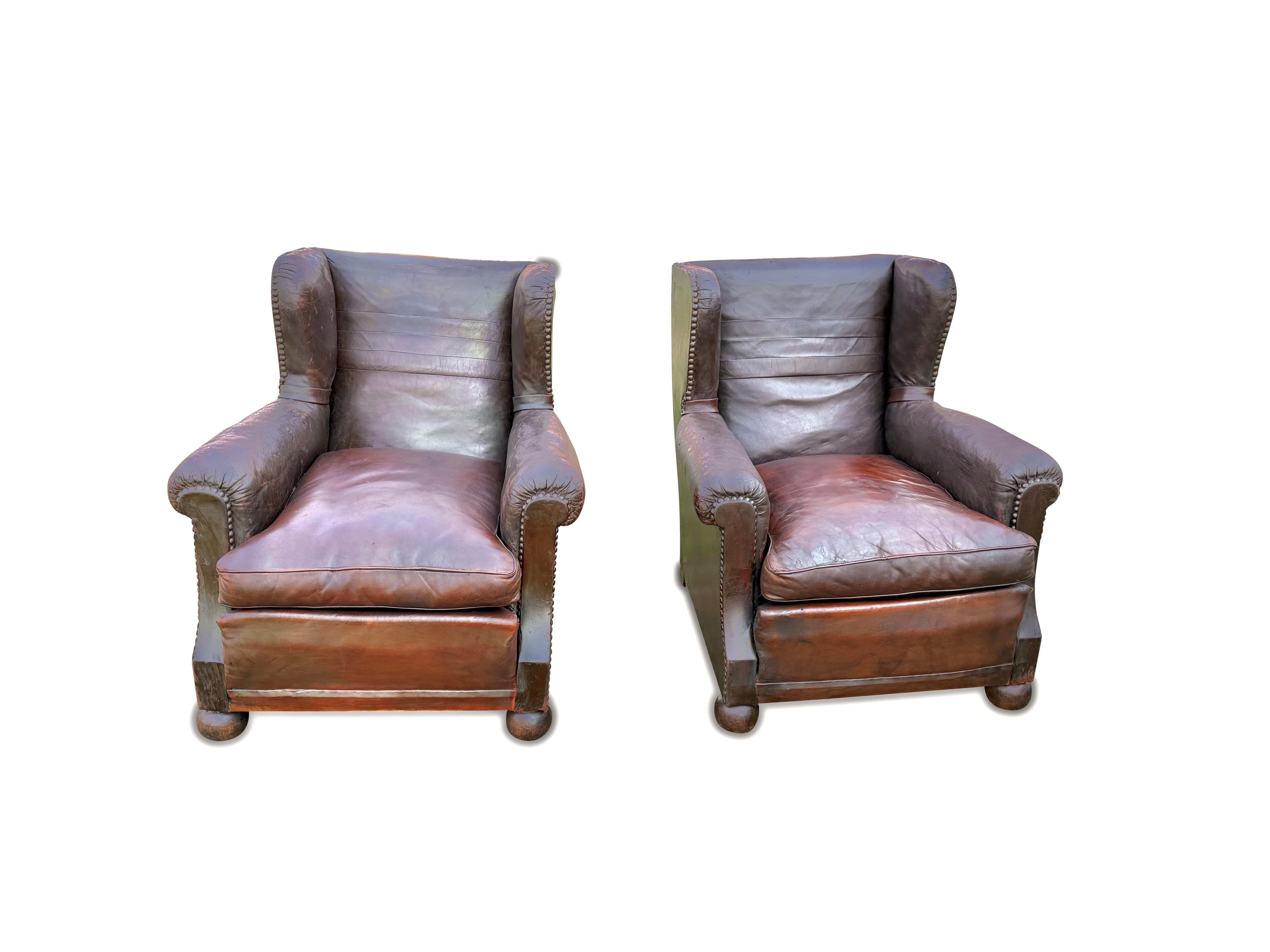 Presenting 1930s classic English wingback leather club armchairs. Featuring elegant nailhead trim along the edges and rounded, solid wood legs for stability.