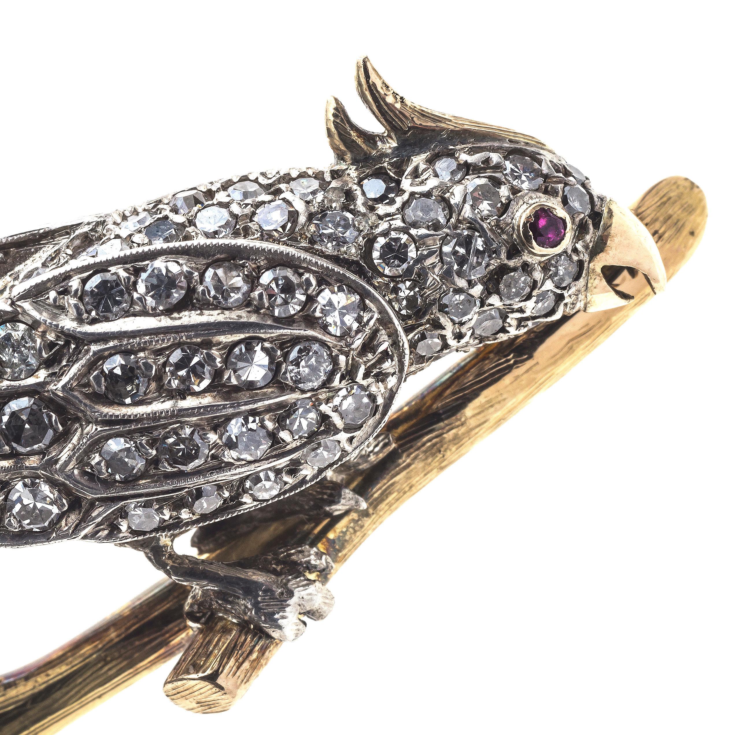 The platinum and 14K yellow gold cockatoo is sitting on an engraved golden branch. The bird has a golden feather bonnet and golden beak, a ruby set in gold is the eye. The platinum body of the cockatoo is completely set with diamonds. The reverse of
