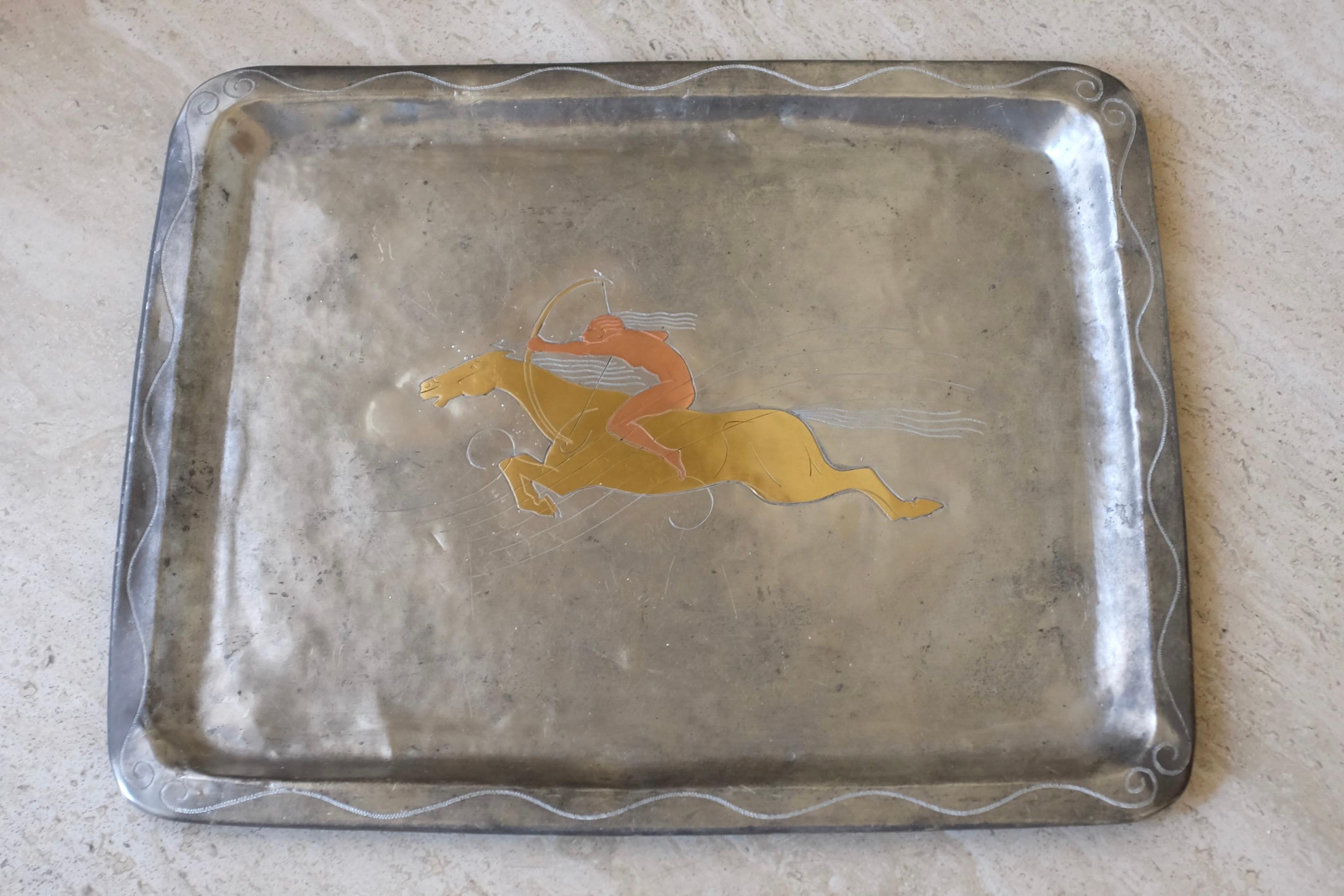 Vassoio in peltro e ottone datato 1930 di Ellen V Kajerdt, Svezia. Forma rettangolare con un'immagine incisa al centro che raffigura una scena di caccia con un uomo a cavallo e una freccia. L'usura del peltro e dell'ottone è dovuta all'età.