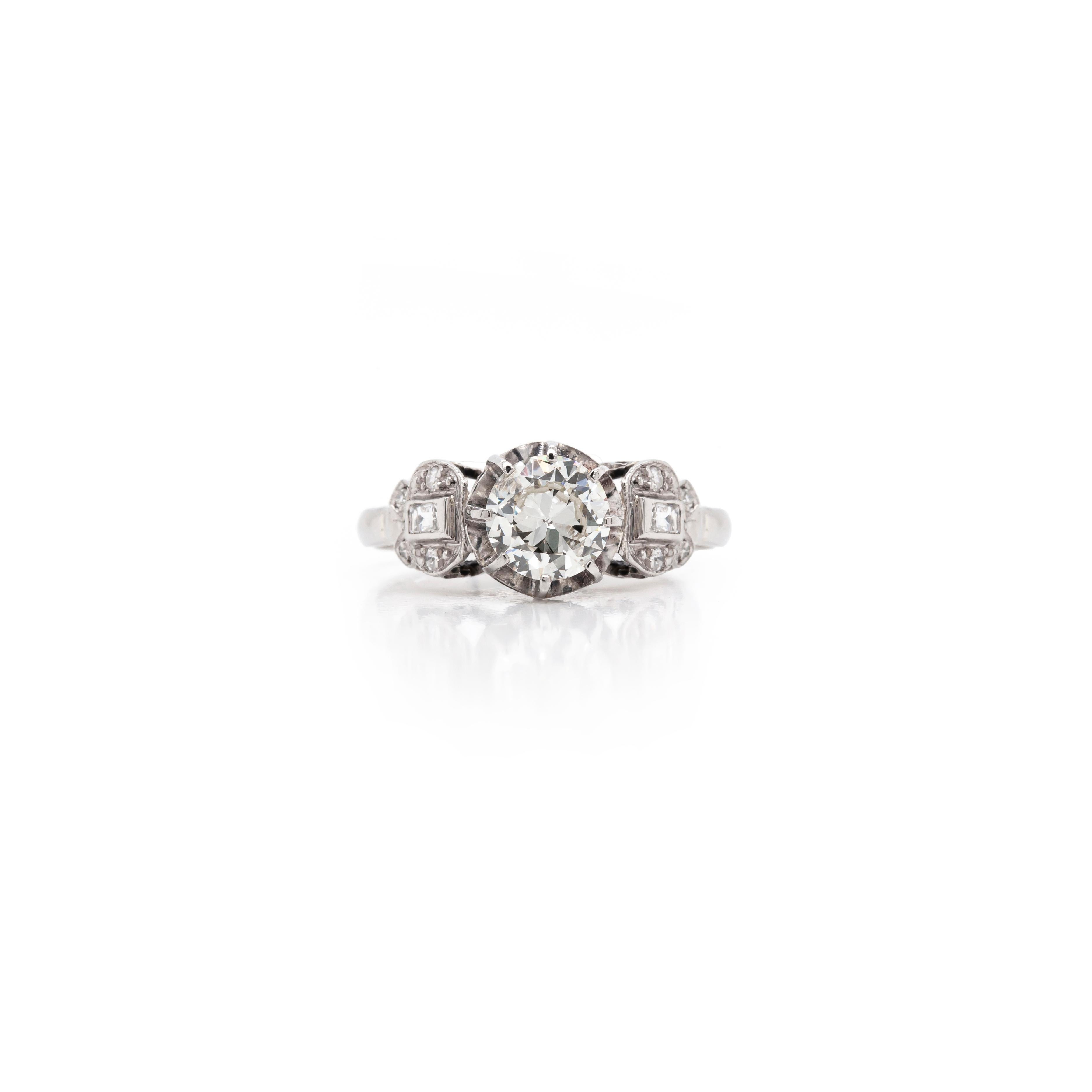 Cette superbe bague de fiançailles des années 1930 présente un magnifique diamant de taille transitionnelle de 1,05 carat au centre, accompagné de part et d'autre d'un diamant de taille baguette serti dans quatre diamants de taille européenne