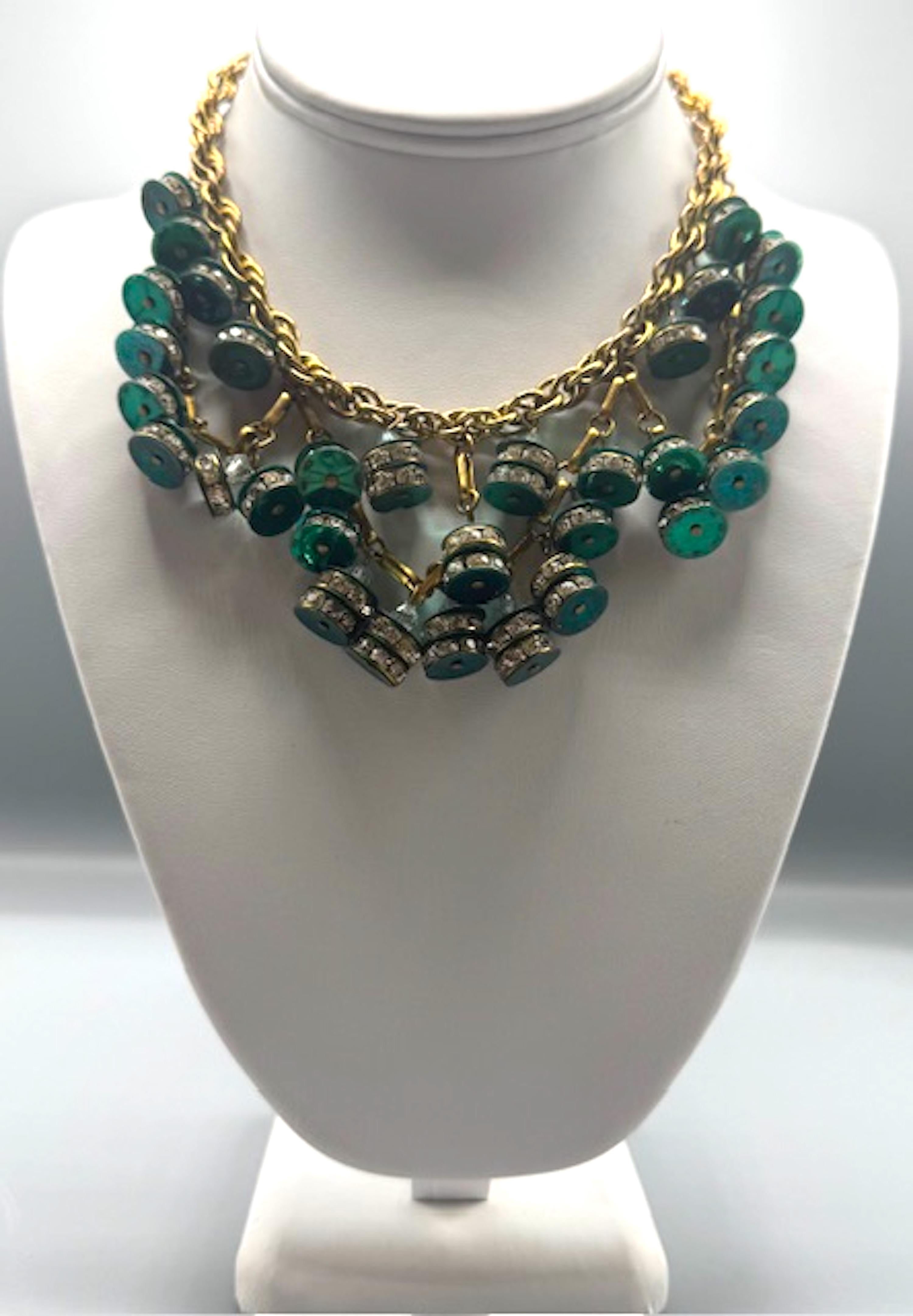 Questa collana è uno splendido pezzo vintage, che unisce l'eleganza dell'epoca Art Déco con i tocchi glamour degli anni Quaranta. La combinazione di ottone placcato oro, rondelle di strass e dischi di plastica verde smeraldo crea un contrasto