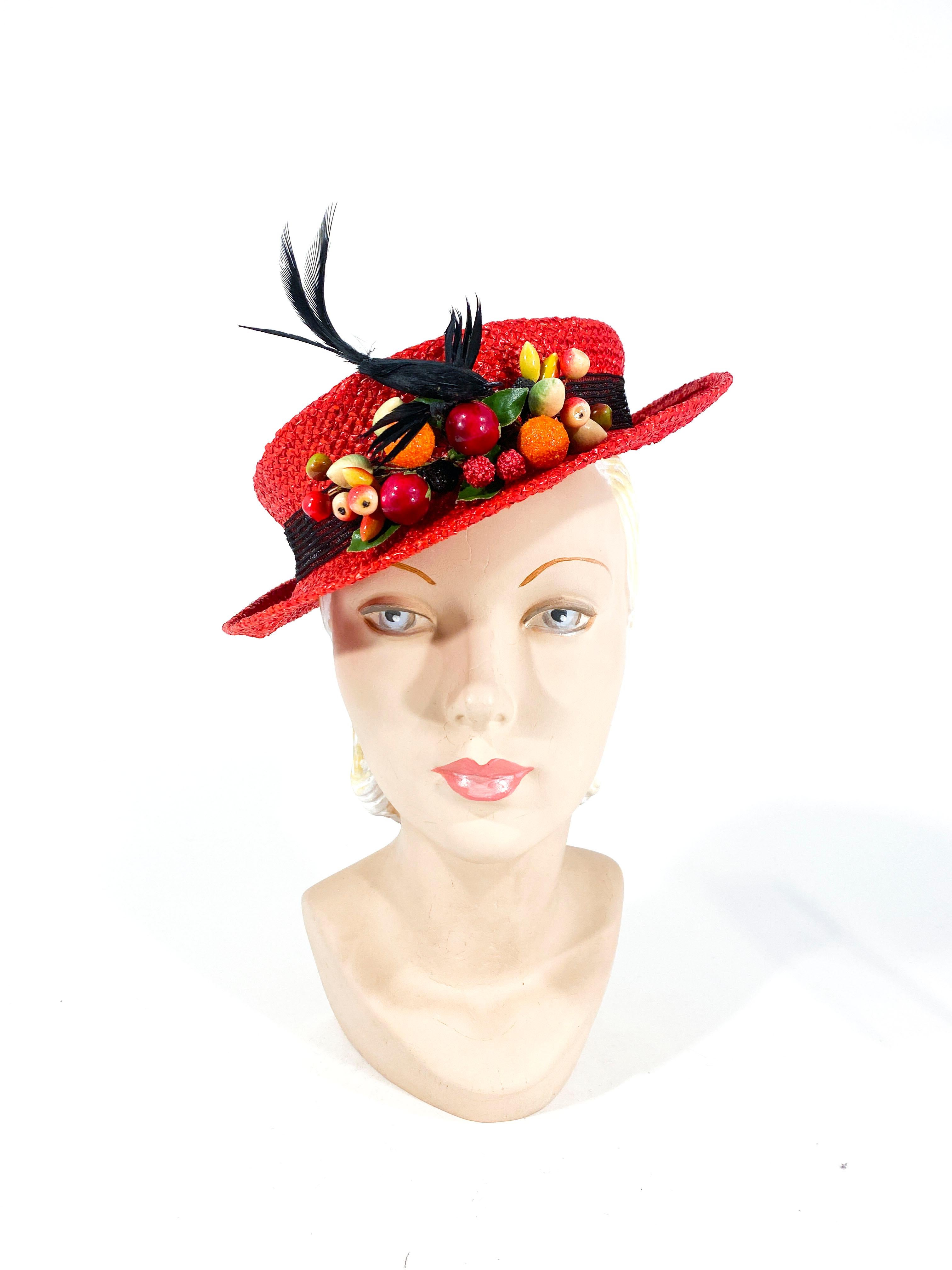 Late 1930's to early 1940's red coated woven straw perch hat decorated with a black mesh band, handcrafted fruit and a feathered sculpted bird.