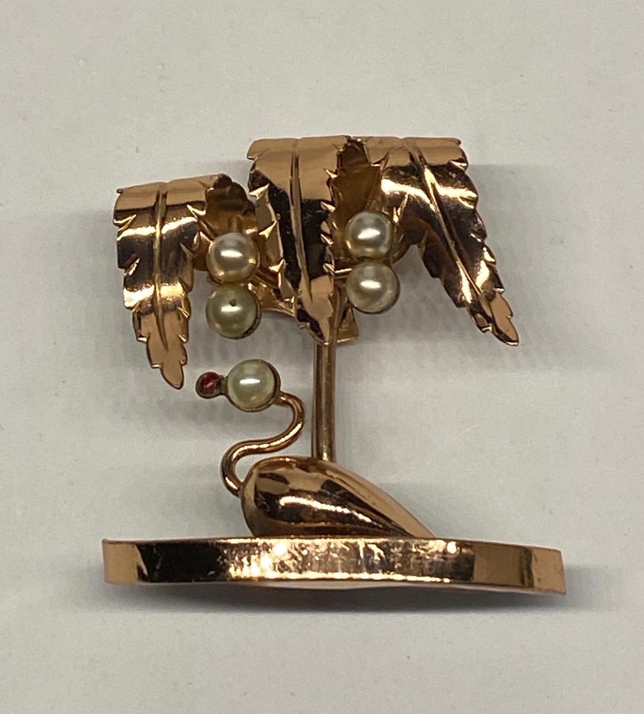A charming Art Deco 1930 to 1940s three dimension figural brooch of a swan swimming under a palm tree. Hand solder construction, rose gold plate and set with six faux glass pearls. The beak of the swan is a small red rhinestone. Attributed to the