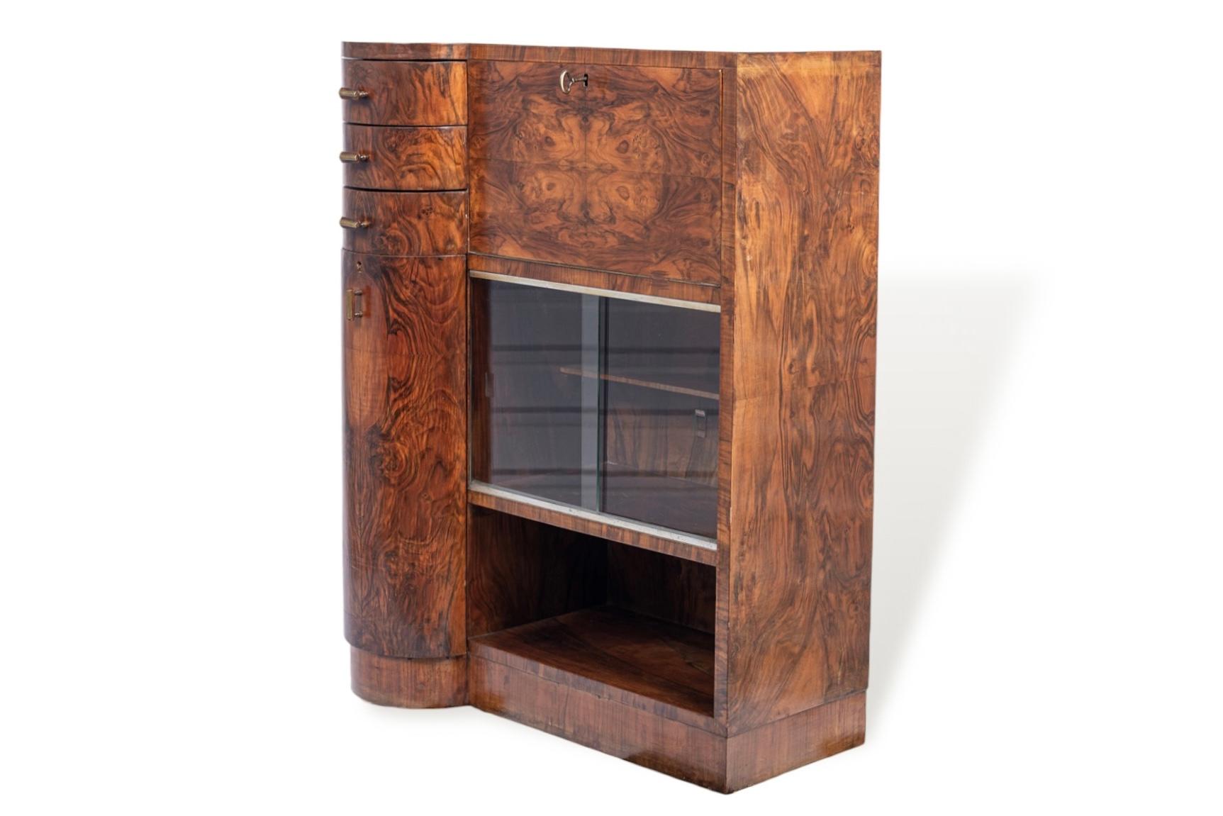 This unique antique Art Deco burl wood and glass secretary desk cabinet is circa 1930. This small cabinet has a distinctive asymmetrical-shaped case and is expertly handcrafted with gorgeous match-booked walnut burl wood grain and finished