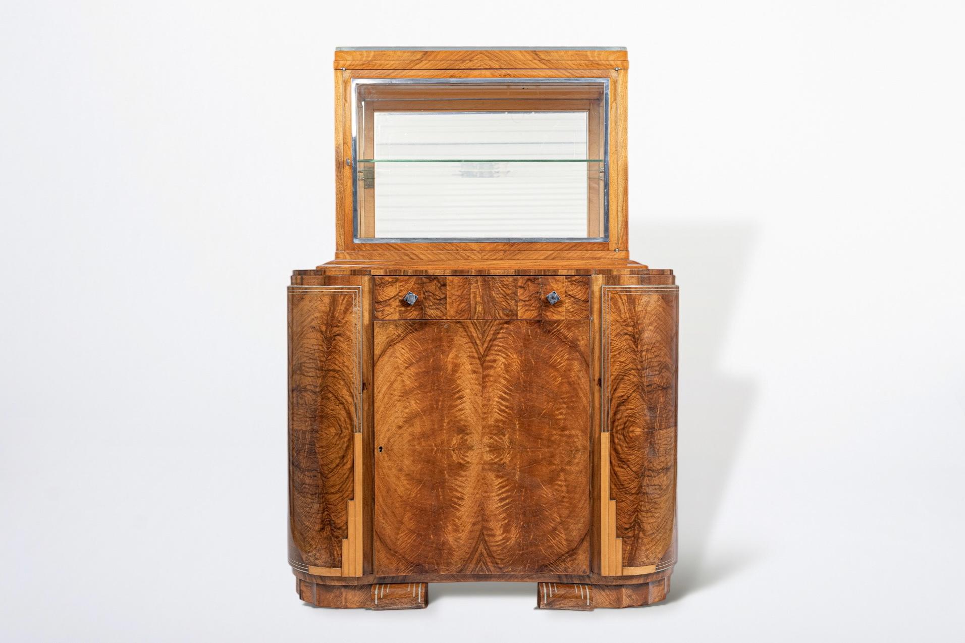 This exquisite antique French Art Deco wood and glass vitrine display cabinet or bar cabinet is circa 1930. It is impeccably handcrafted from high quality materials including solid wood and mahogany crotched veneer with gorgeous grain patterning and