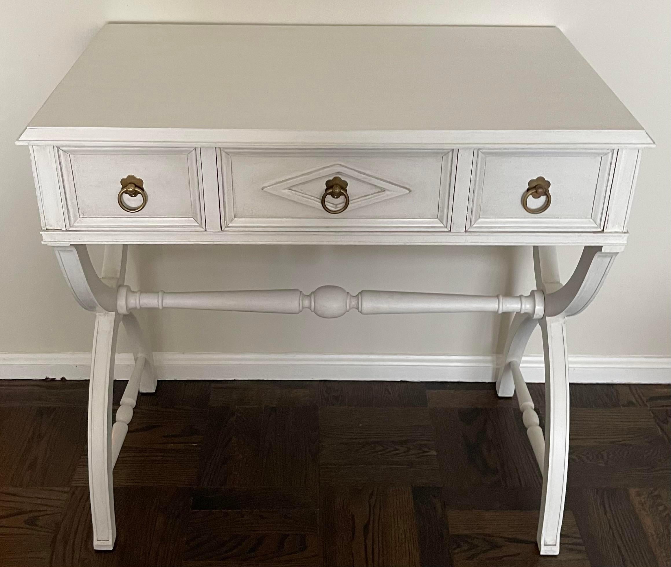 1930s neoclassical writing table or vanity table. Newly painted in an antique white finish. New vintage brass ring pulls have overall unpolished patina.
Clearance from floor to bottom of drawers is 24” tall.