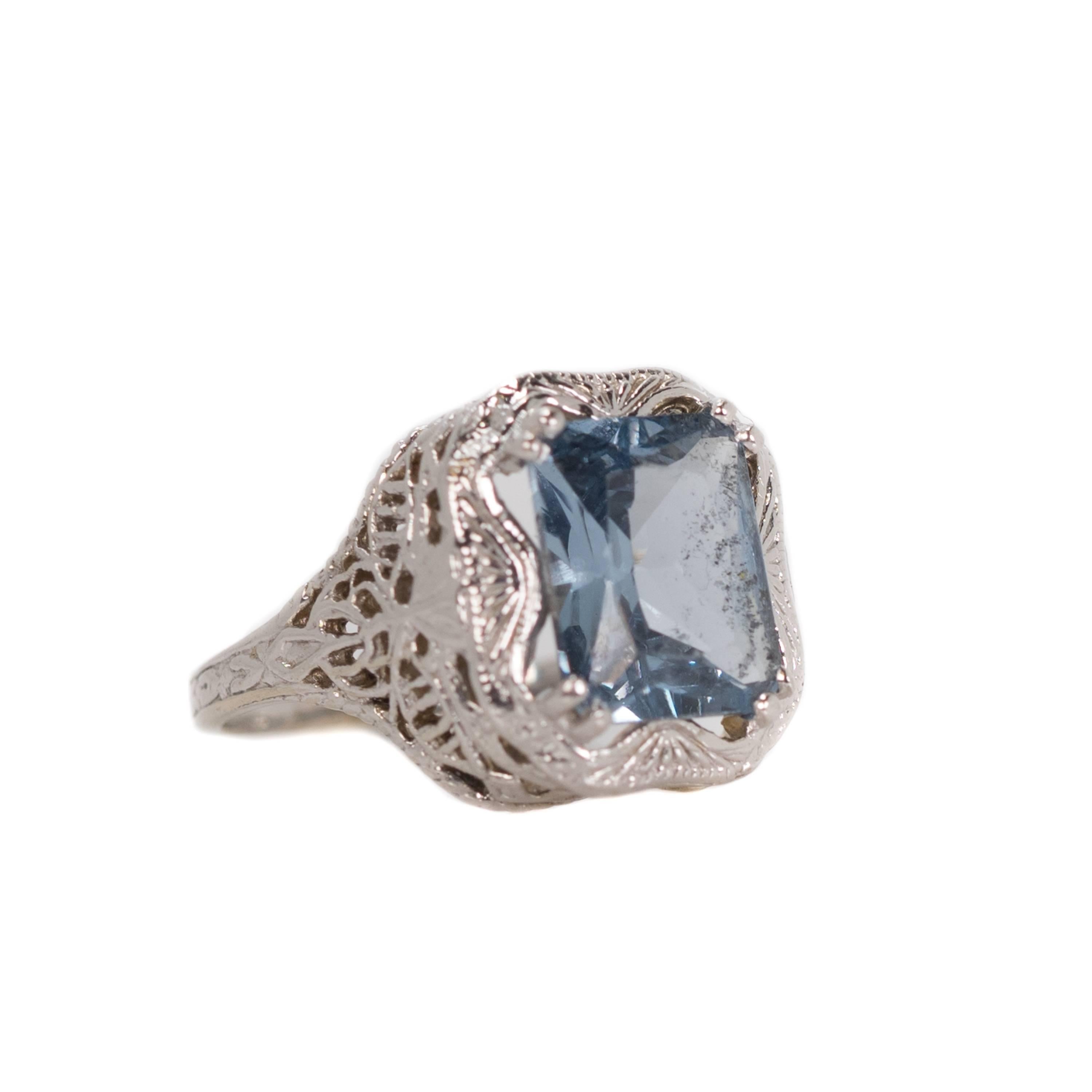 1930s Art Deco Emerald cut Aqua Glass & 14k White Gold Filigree Ring

Features a light to medium Aqua blue Glass center stone. The Emerald cut stone is held securely in place with 4 double talon prongs. The center stone is surrounded by a