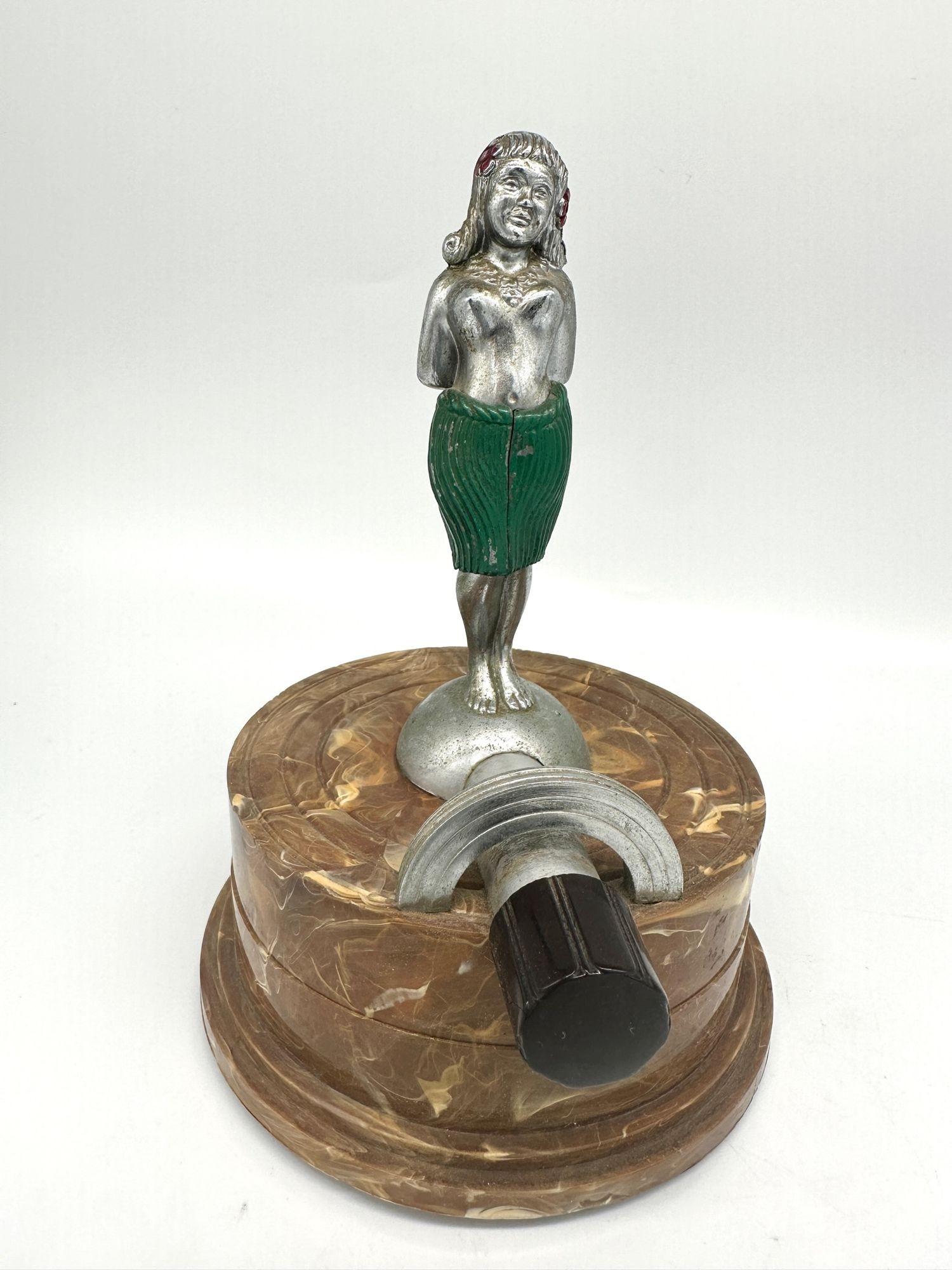 This vintage table lighter by the company ARROW is an exceedingly rare find: a tastefully nude Hula Girl model crafted from chromed metal, featuring a Bakelite base. Within the base lies an innovative silent flame lighter, showcasing early